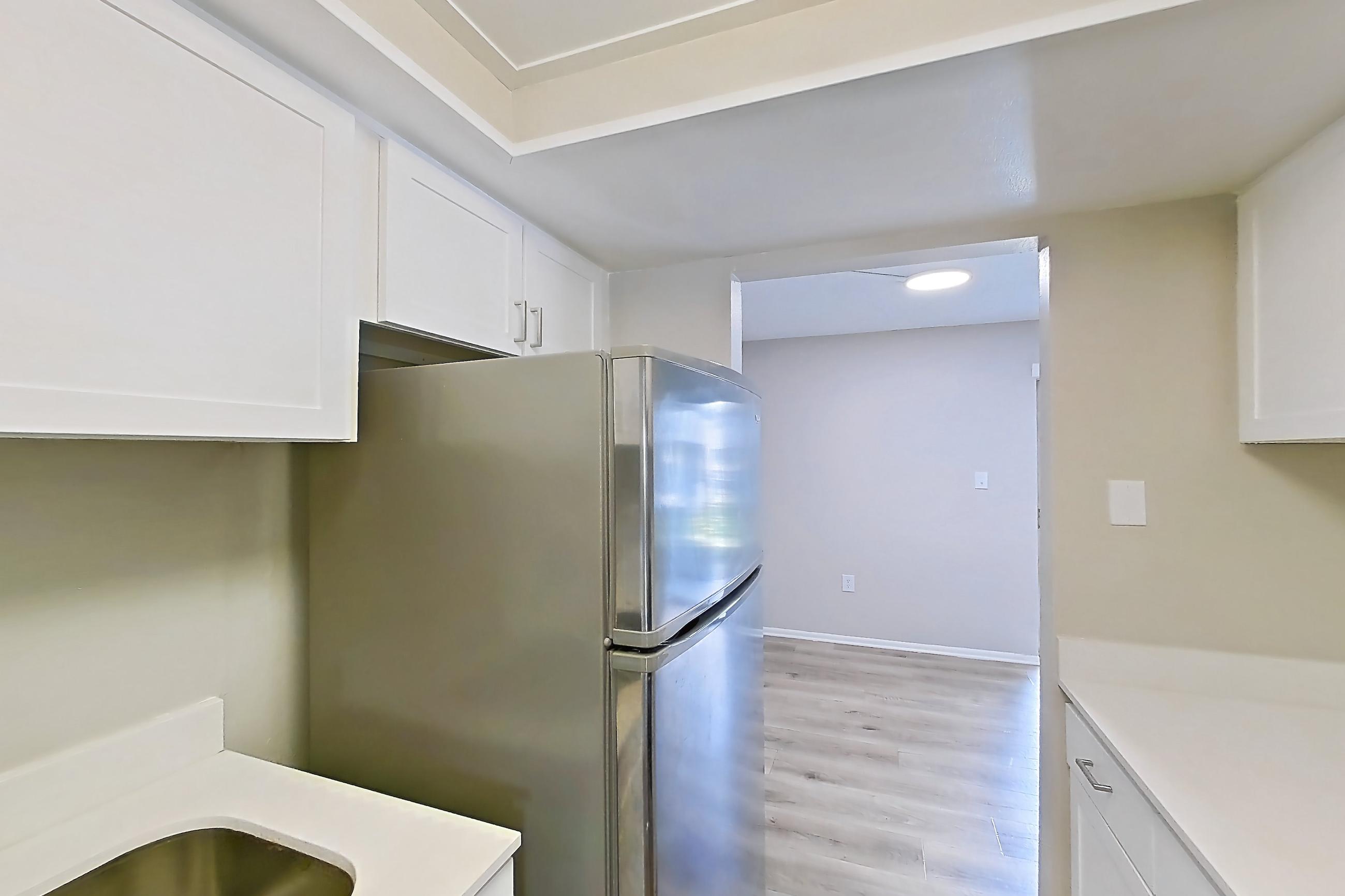 Kitchen with black appliances, dishwasher, electric range, light countertops, light wood-finish flooring, oven/range, range hood, refrigerator, stainless steel appliances, and white appliances, Apartment 315 at Venue at Winter Park