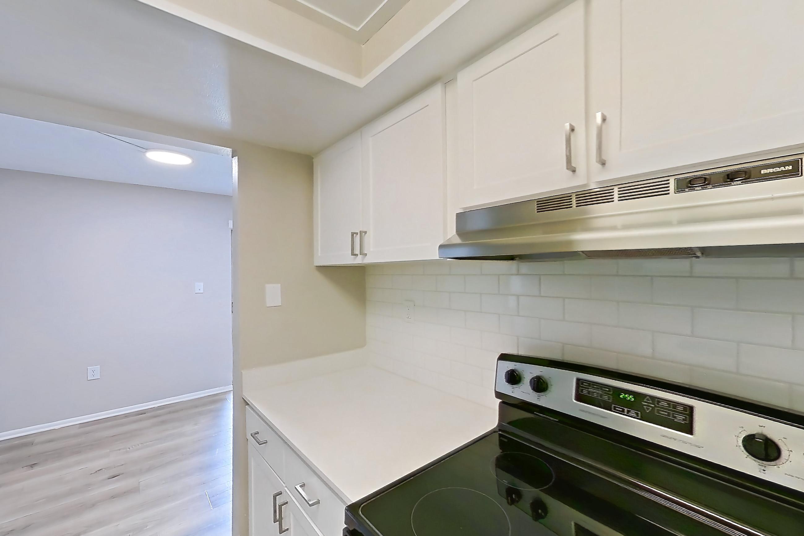 Kitchen with black appliances, dishwasher, electric range, light countertops, light wood-finish flooring, oven/range, range hood, refrigerator, stainless steel appliances, and white appliances, Apartment 315 at Venue at Winter Park