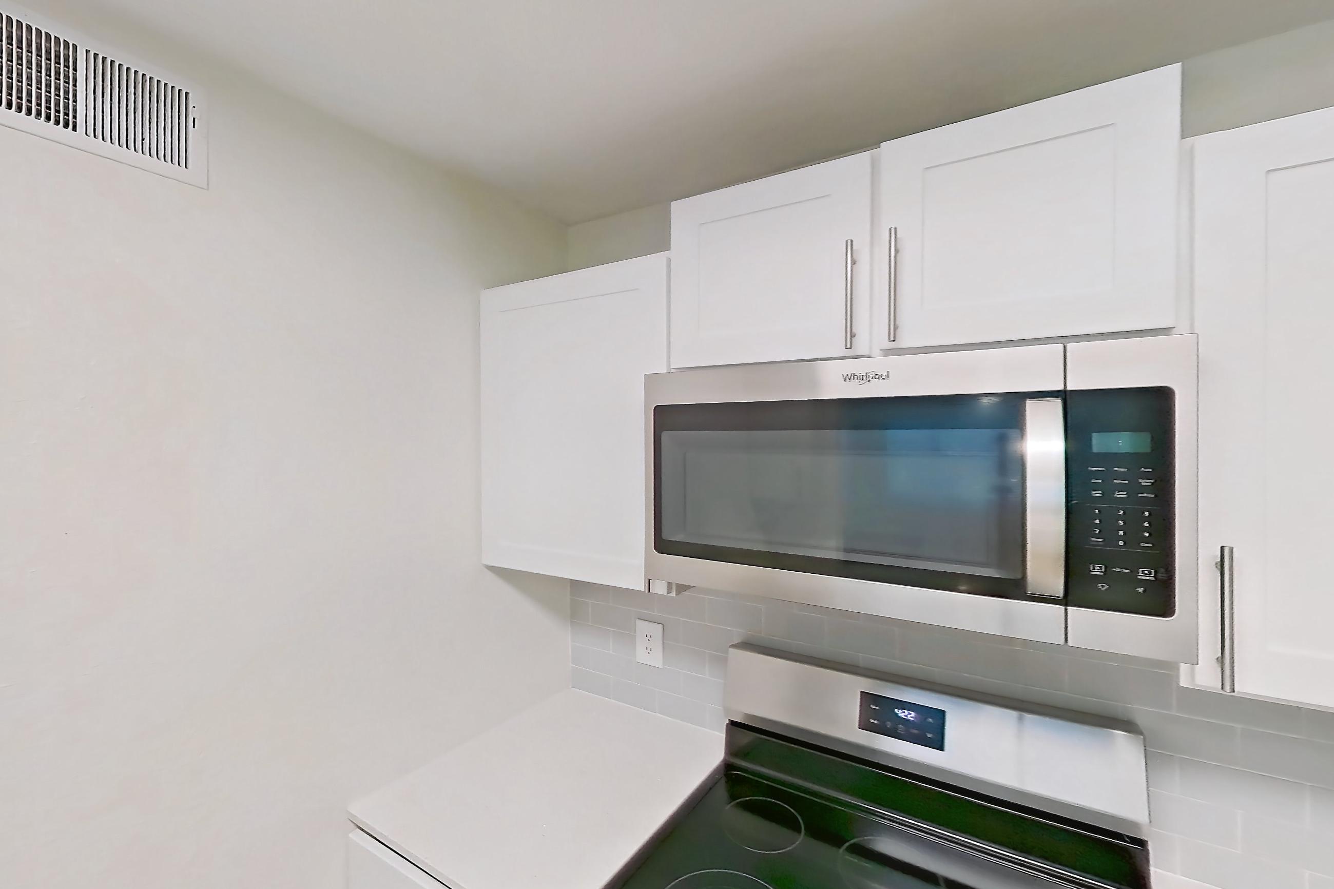 Kitchen with dishwasher, electric range, light countertops, light stone countertops, light wood-finish flooring, microwave, oven/range, refrigerator, and stainless steel appliances, Apartment 14-204 at Boot Ranch