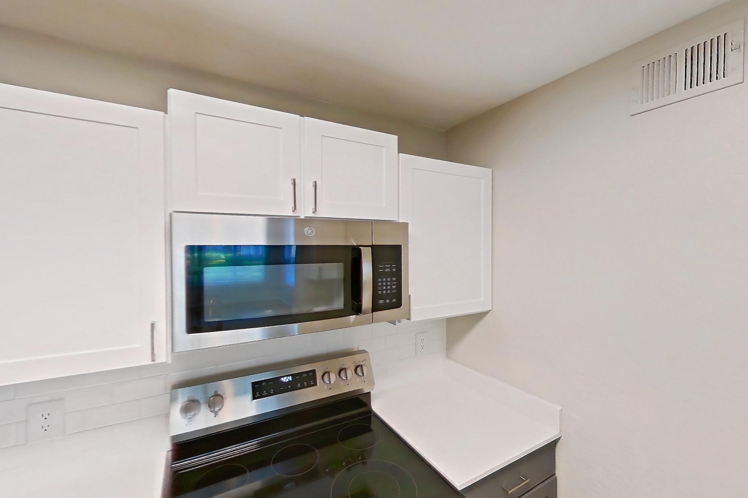 Kitchen with dishwasher, electric range, light countertops, light wood-finish flooring, microwave, oven/range, refrigerator, and stainless steel appliances, Apartment 15-102 at Boot Ranch
