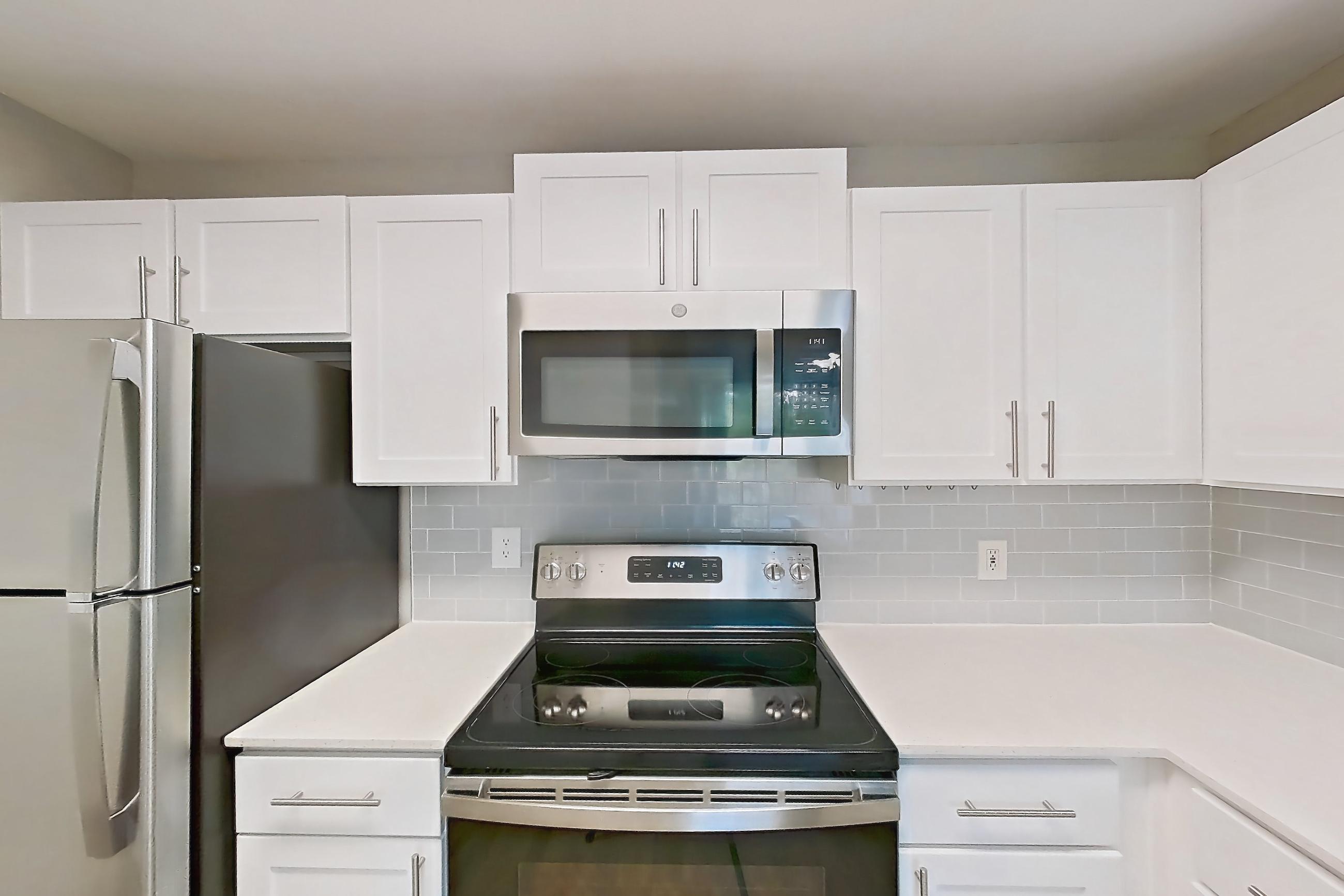 Kitchen with black appliances, dishwasher, electric range, light countertops, light stone countertops, light wood-finish flooring, microwave, oven/range, refrigerator, stainless steel appliances, and white appliances, Apartment 16-301 at Boot Ranch