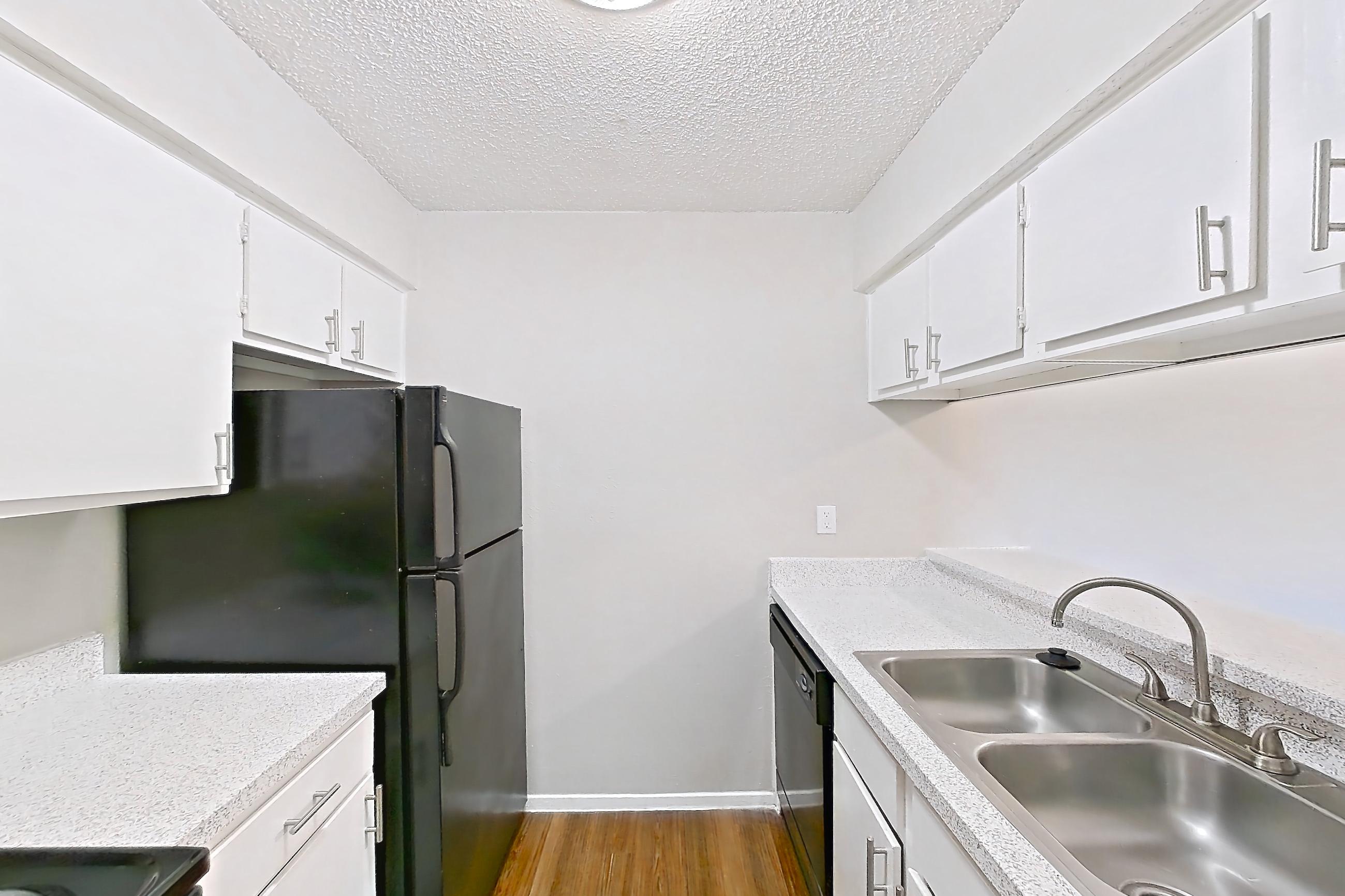 Kitchen with black appliances, dark wood-finish flooring, dishwasher, electric range, light countertops, light stone countertops, oven/range, range hood, and refrigerator, Apartment 1002 at Westgate