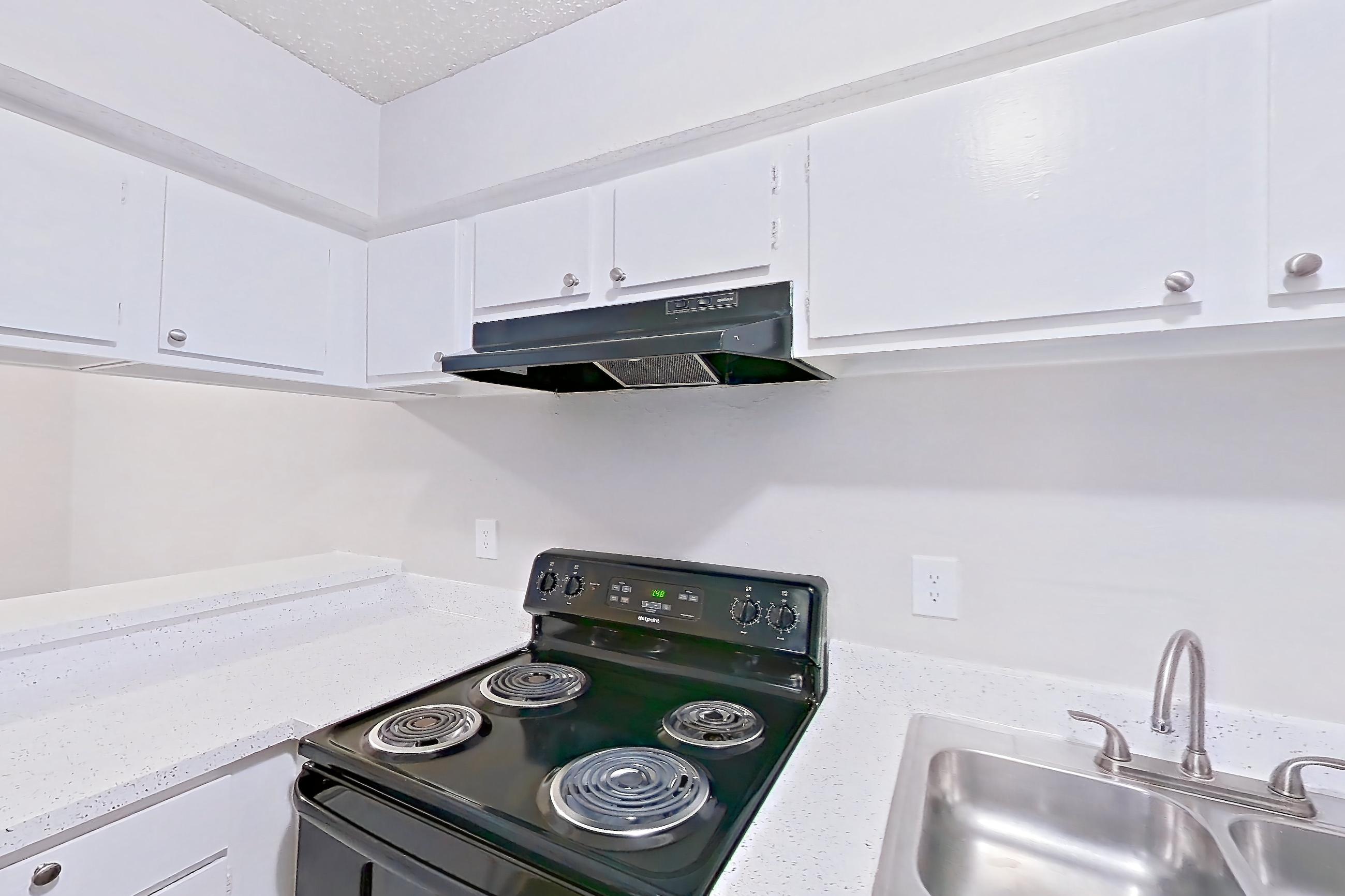 Kitchen with black appliances, electric range, light countertops, light stone countertops, light wood-finish flooring, oven/range, range hood, refrigerator, and wood-look tile flooring, Apartment 1101 at Westgate
