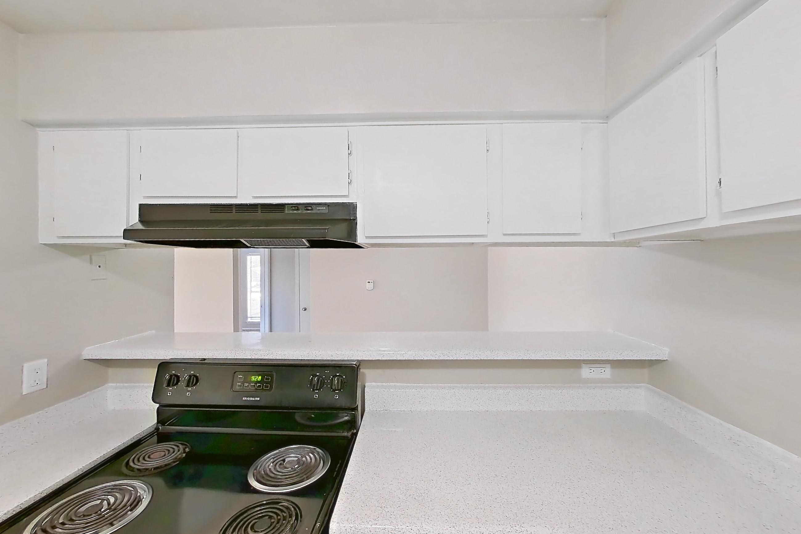 Kitchen with black appliances, electric range, light countertops, light stone countertops, light wood-finish flooring, oven/range, range hood, and refrigerator, Apartment 2328 at Westgate