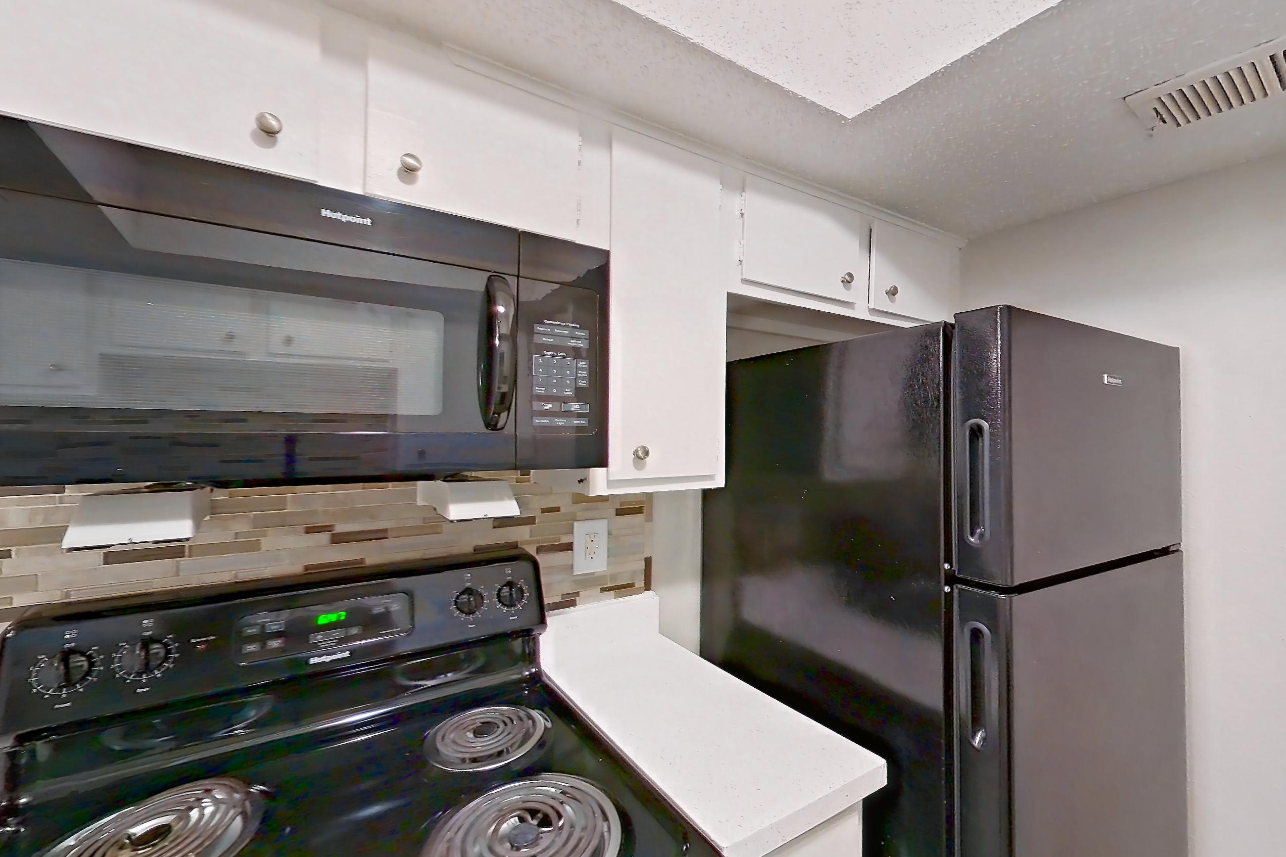 Kitchen with black appliances, dishwasher, electric range, light carpet, light countertops, light stone countertops, light wood-finish flooring, microwave, oven/range, and refrigerator, Apartment 2013 at Enclave at Prestonwood
