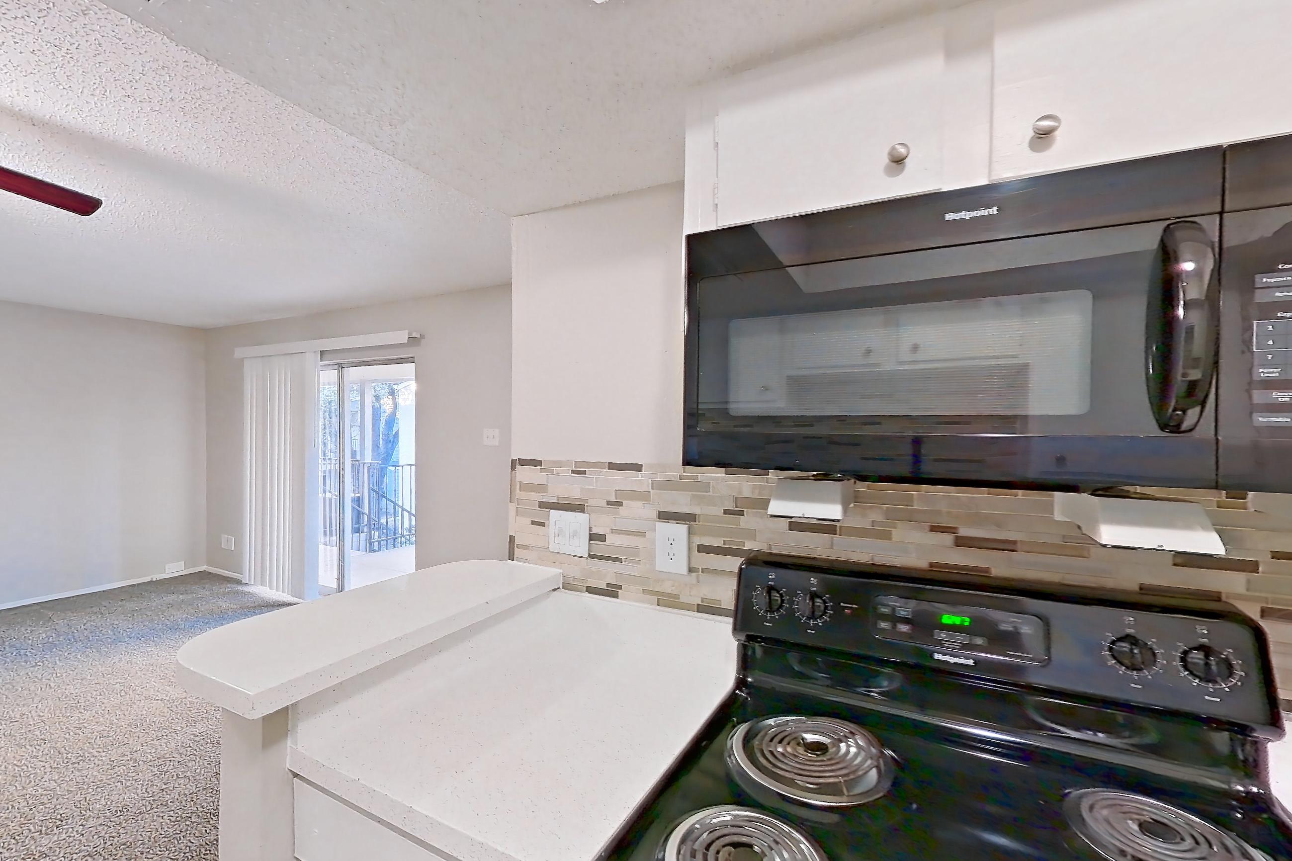 Kitchen with black appliances, dishwasher, electric range, light carpet, light countertops, light stone countertops, light wood-finish flooring, microwave, oven/range, and refrigerator, Apartment 2013 at Enclave at Prestonwood