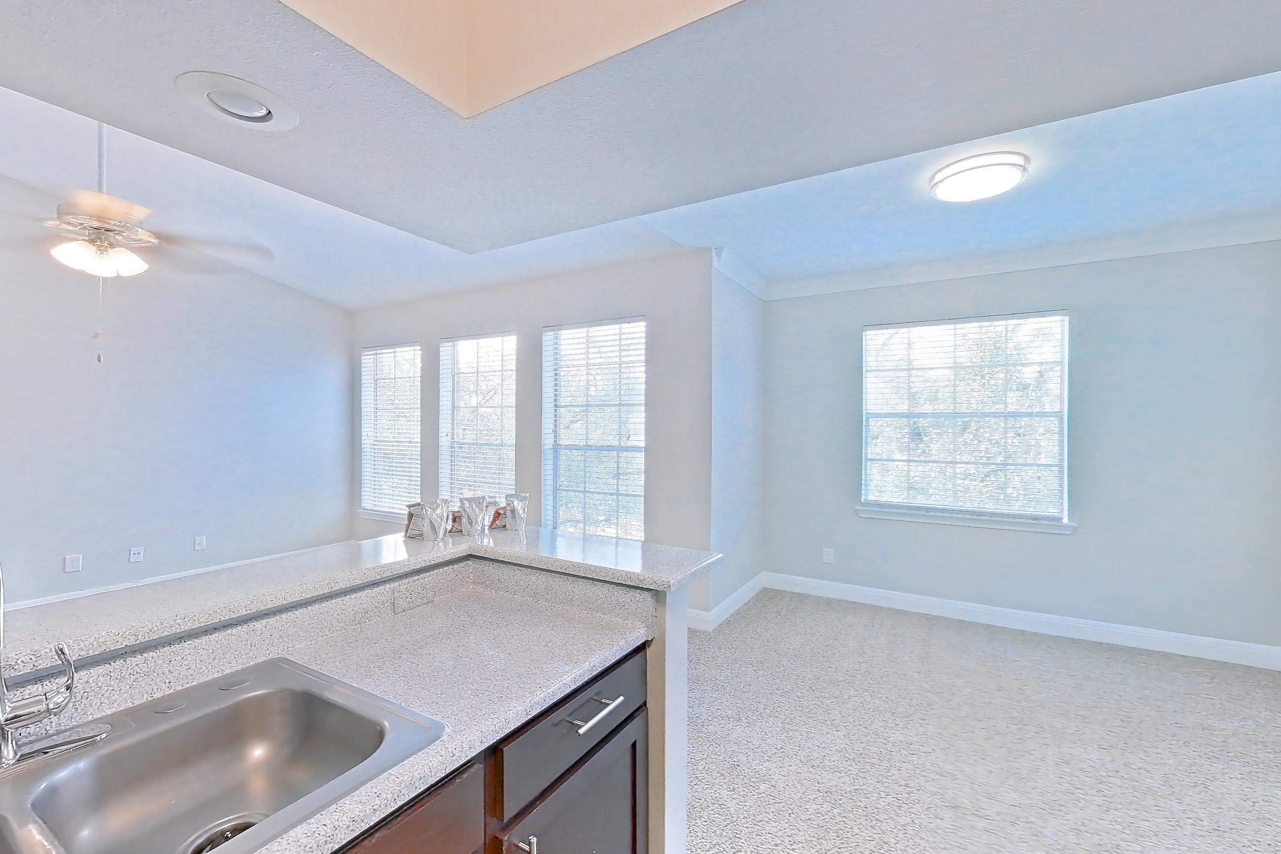 Kitchen with black appliances, dishwasher, electric range, light carpet, light countertops, light stone countertops, light wood-finish flooring, oven/range, refrigerator, and stainless steel appliances, Unit 0216 at Champions Park