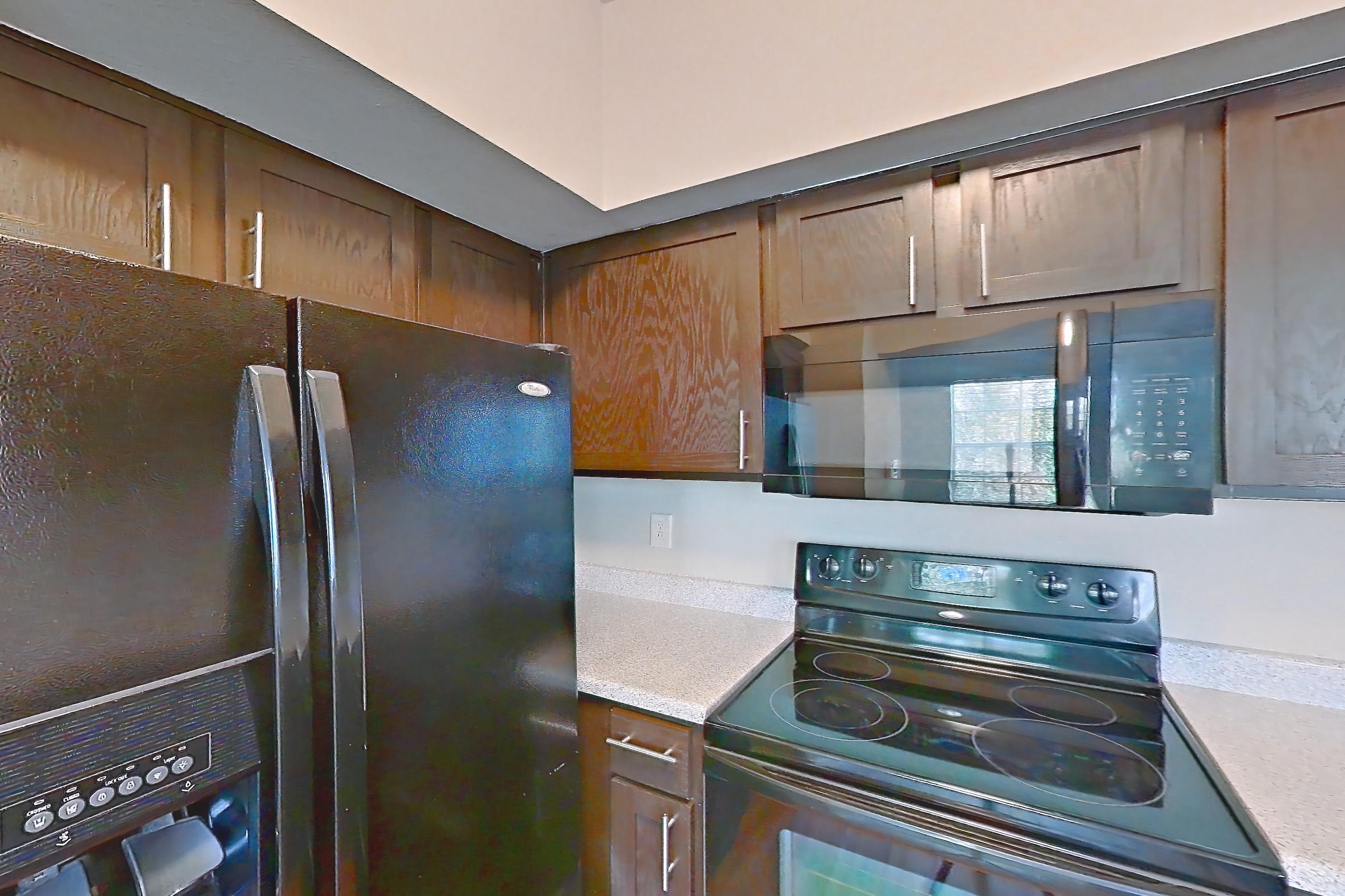 Kitchen with black appliances, dishwasher, electric range, light carpet, light countertops, light stone countertops, light wood-finish flooring, oven/range, refrigerator, and stainless steel appliances, Unit 0216 at Champions Park