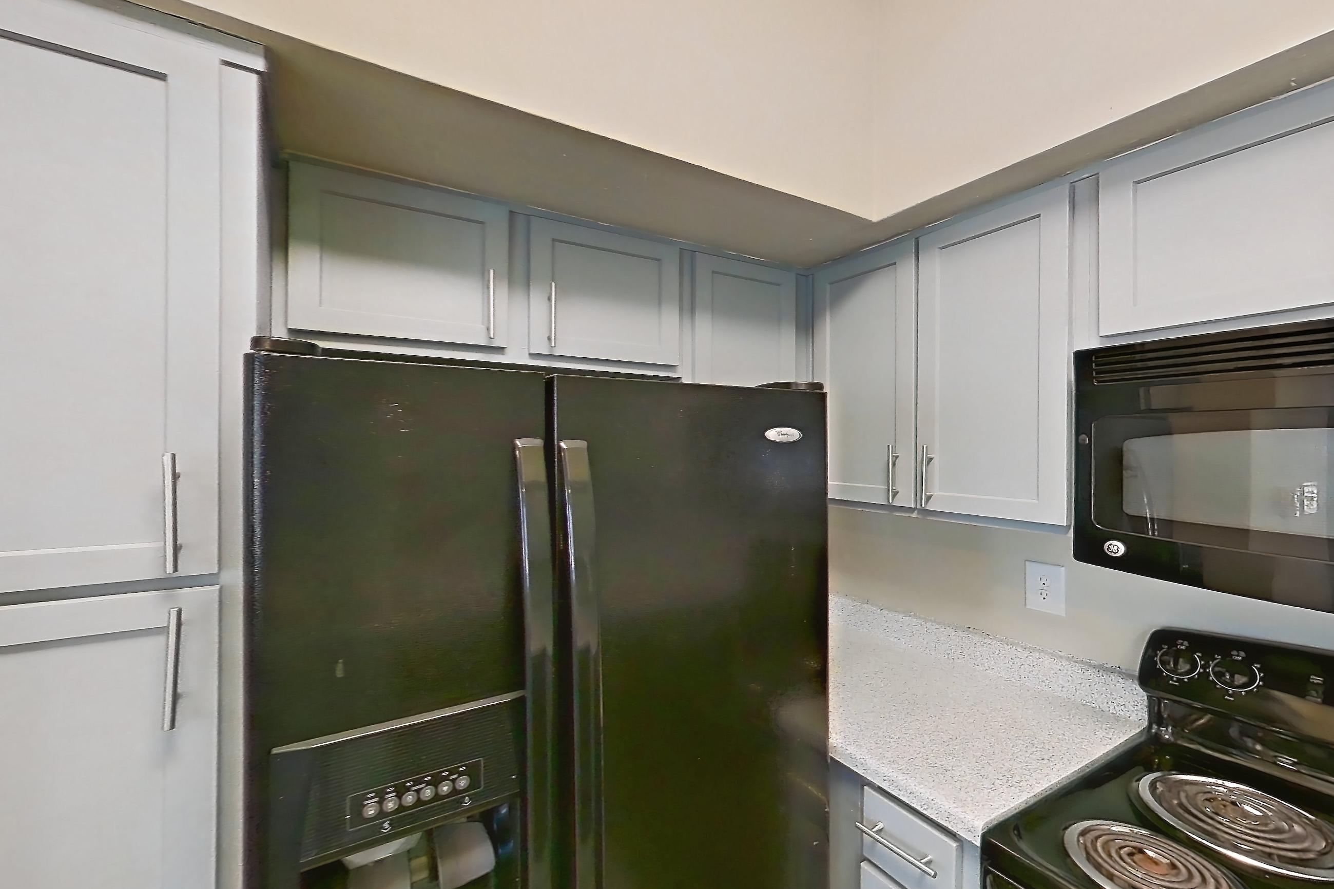 Kitchen with black appliances, dishwasher, light countertops, light stone countertops, light wood-finish flooring, oven/range, refrigerator, water & ice dispenser, and wood-look tile flooring, Apartment 0308 at Champions Park