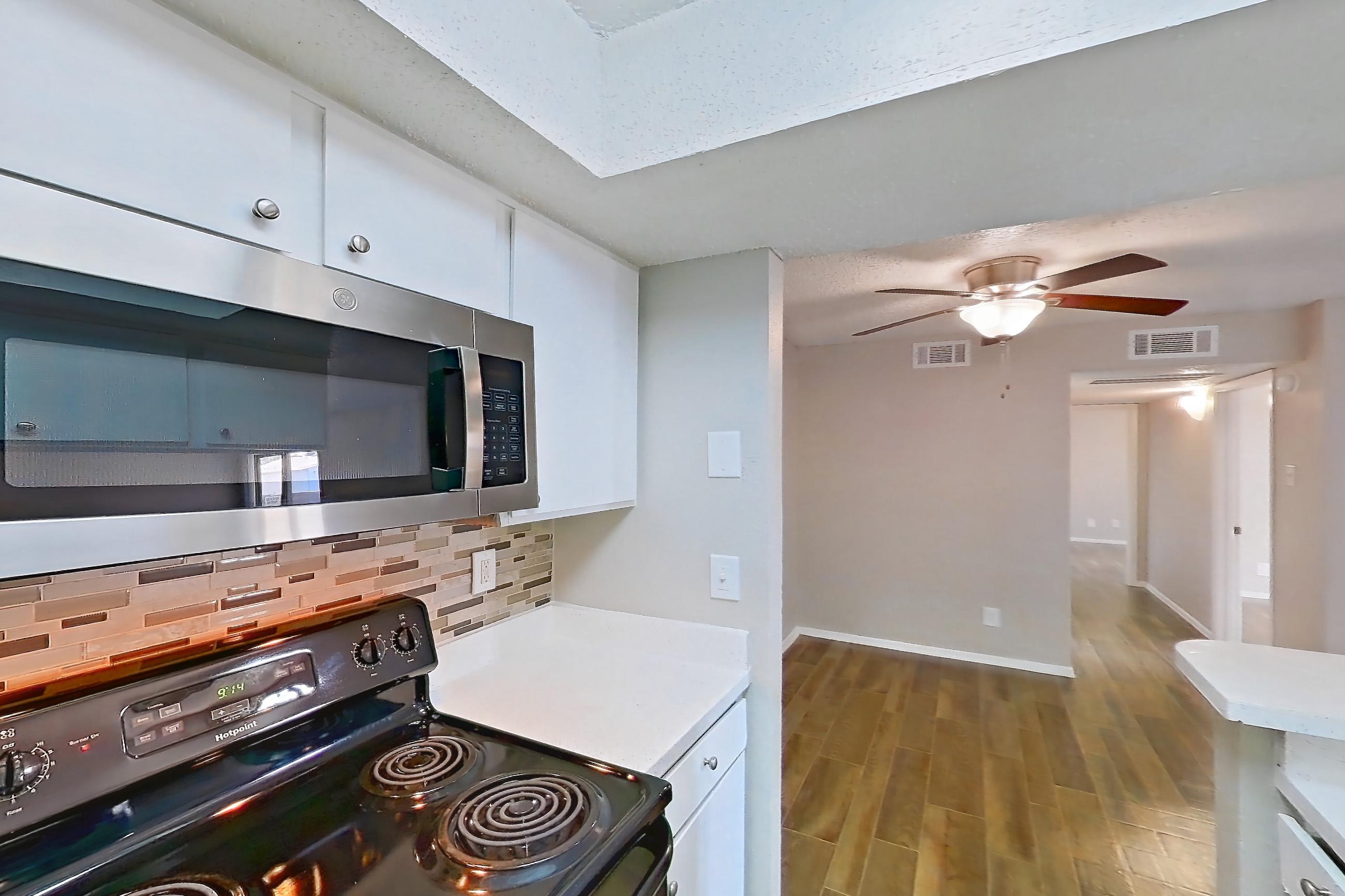 Kitchen with black appliances, dishwasher, electric range, fireplace, light countertops, light wood-finish flooring, oven/range, refrigerator, stainless steel appliances, and wood-look tile flooring, Apartment 1156 at Enclave at Prestonwood