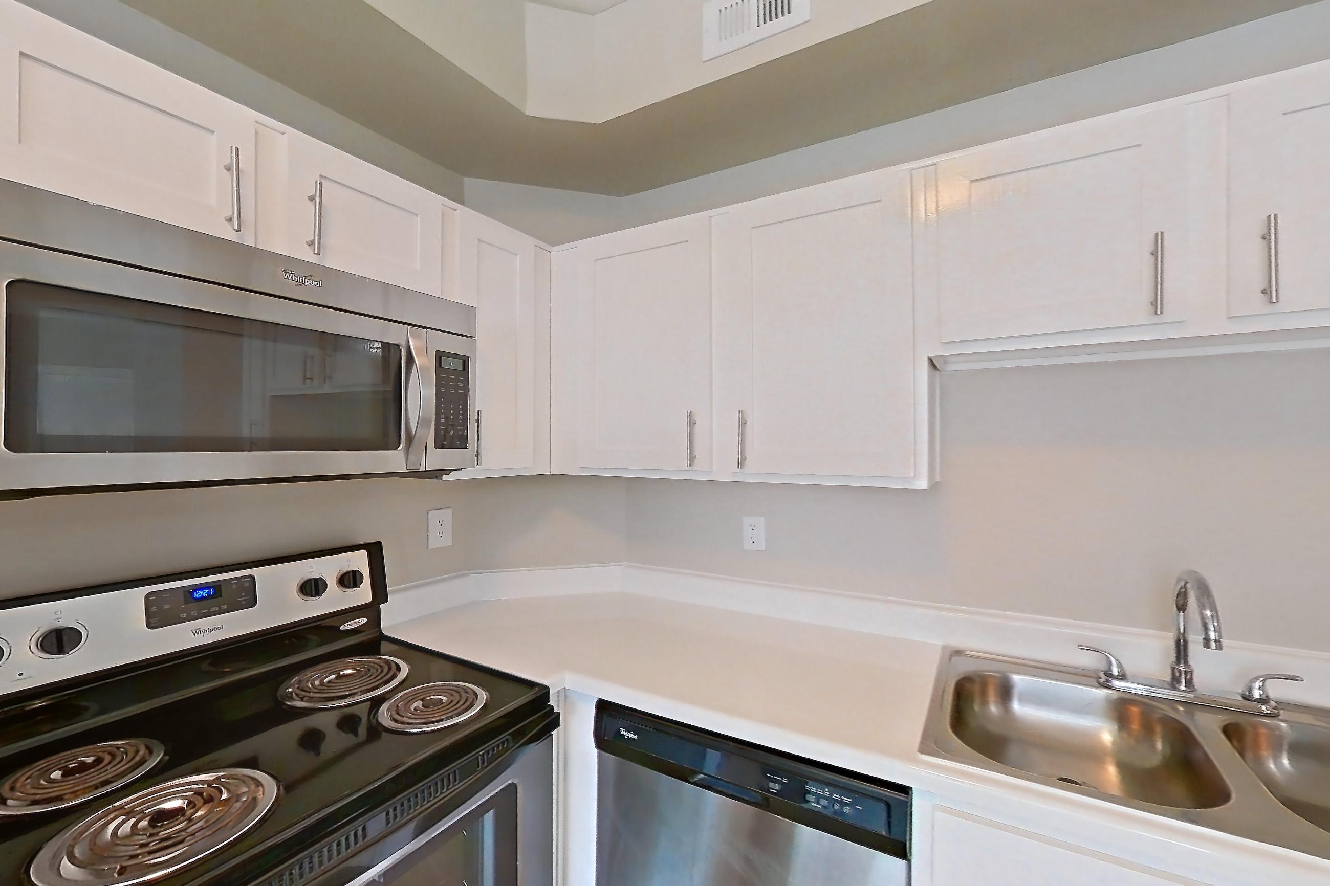 Kitchen with dark wood-finish flooring, dishwasher, electric range, light countertops, light wood-finish flooring, oven/range, refrigerator, stainless steel appliances, and wood-look tile flooring, Apartment 805 at Champions Centre