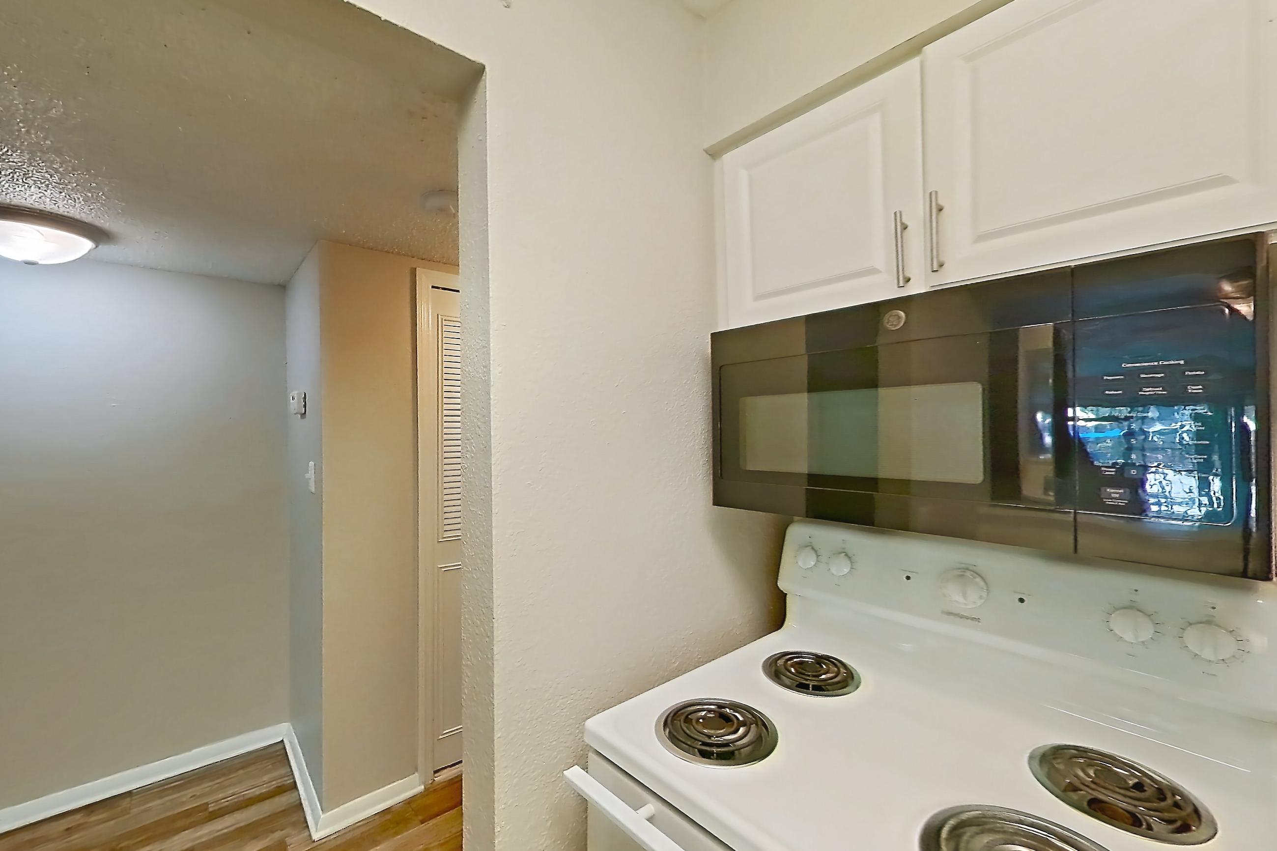 Kitchen with black appliances, electric range, light stone countertops, light wood-finish flooring, microwave, oven/range, and white appliances, Apartment C-08 at Sunset Place