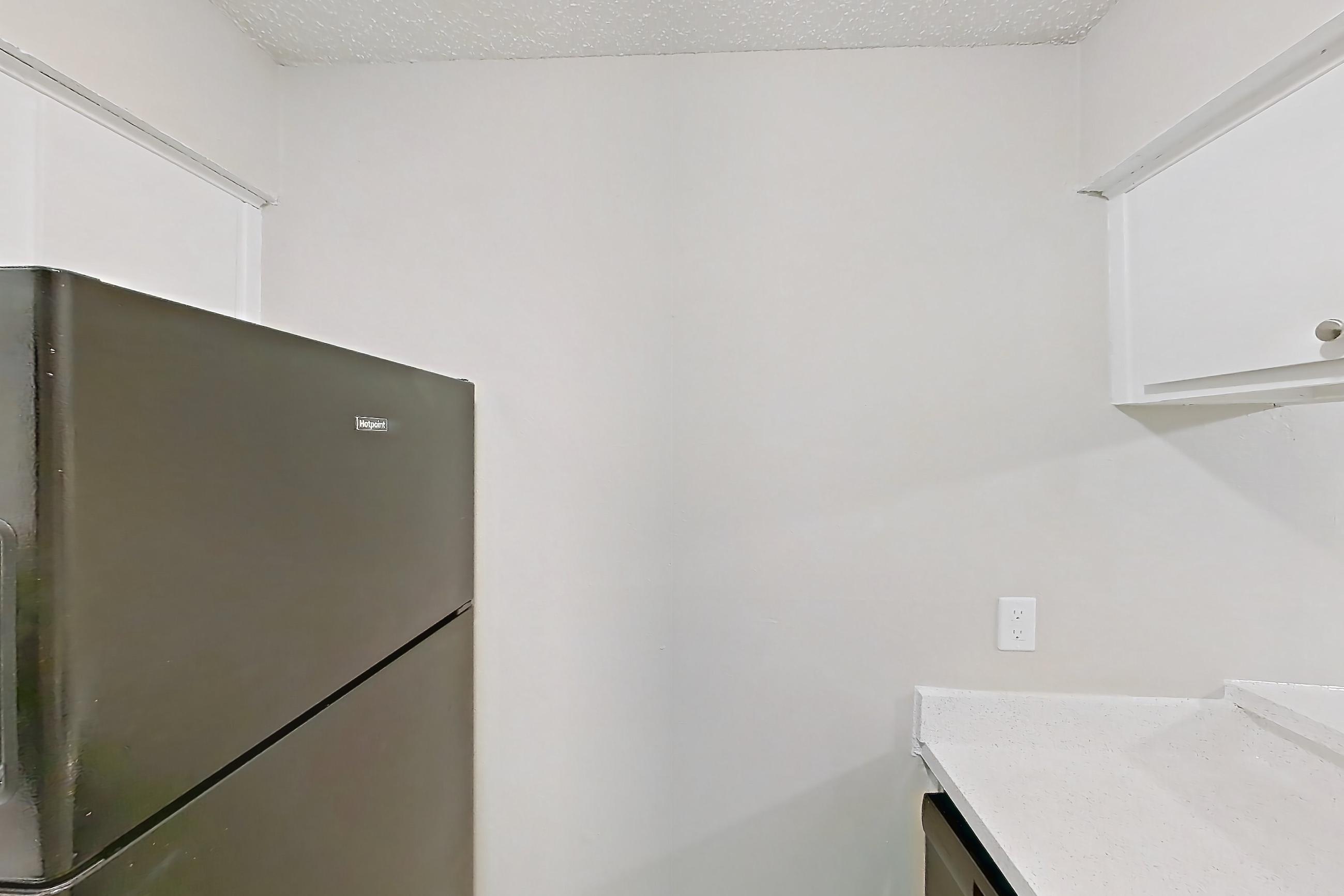 Kitchen with black appliances, dishwasher, electric range, light countertops, light stone countertops, light wood-finish flooring, oven/range, range hood, refrigerator, and stainless steel appliances, Apartment 809 at Westgate