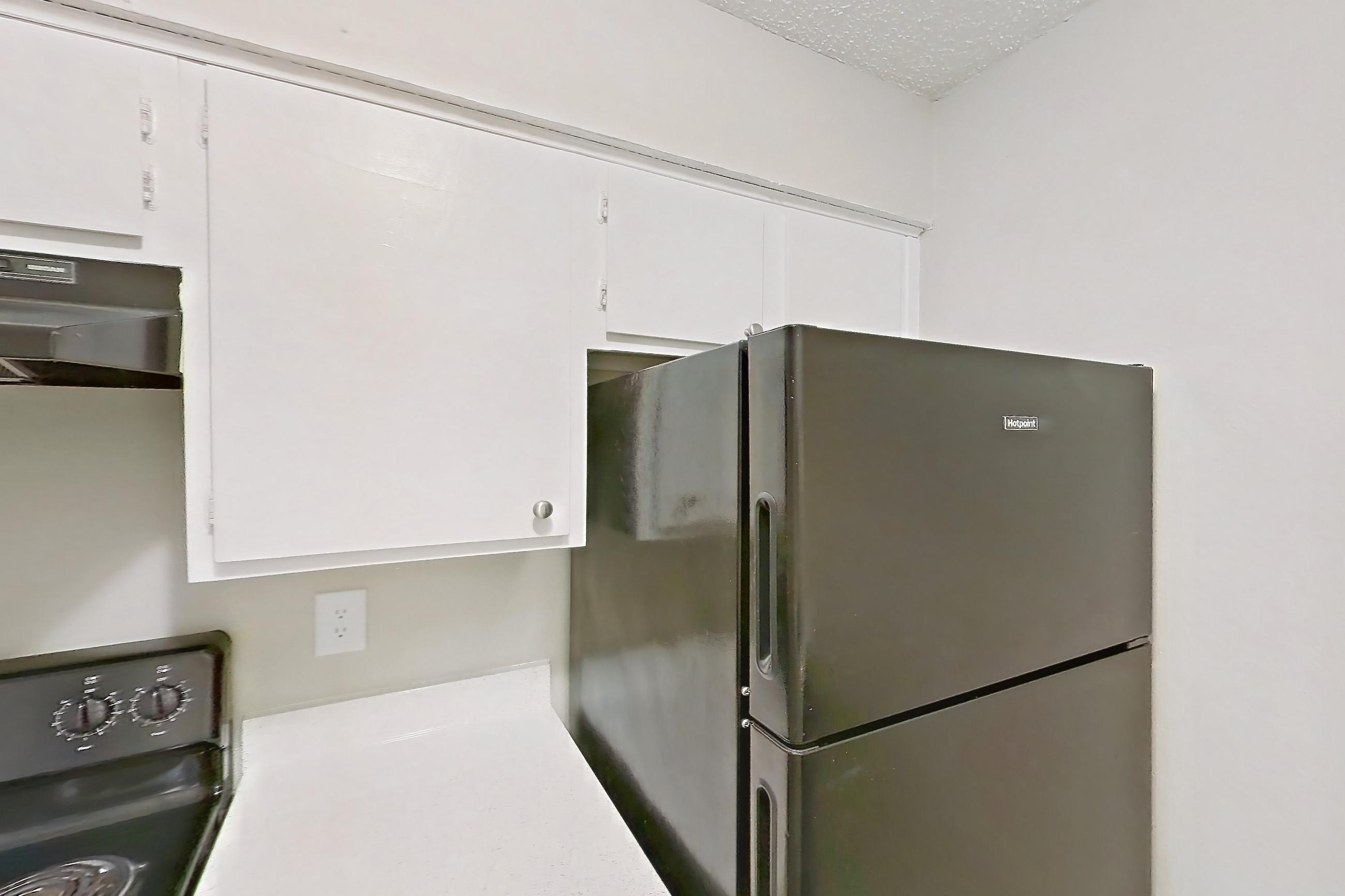 Kitchen with black appliances, dishwasher, electric range, light countertops, light stone countertops, light wood-finish flooring, oven/range, range hood, refrigerator, and stainless steel appliances, Apartment 809 at Westgate