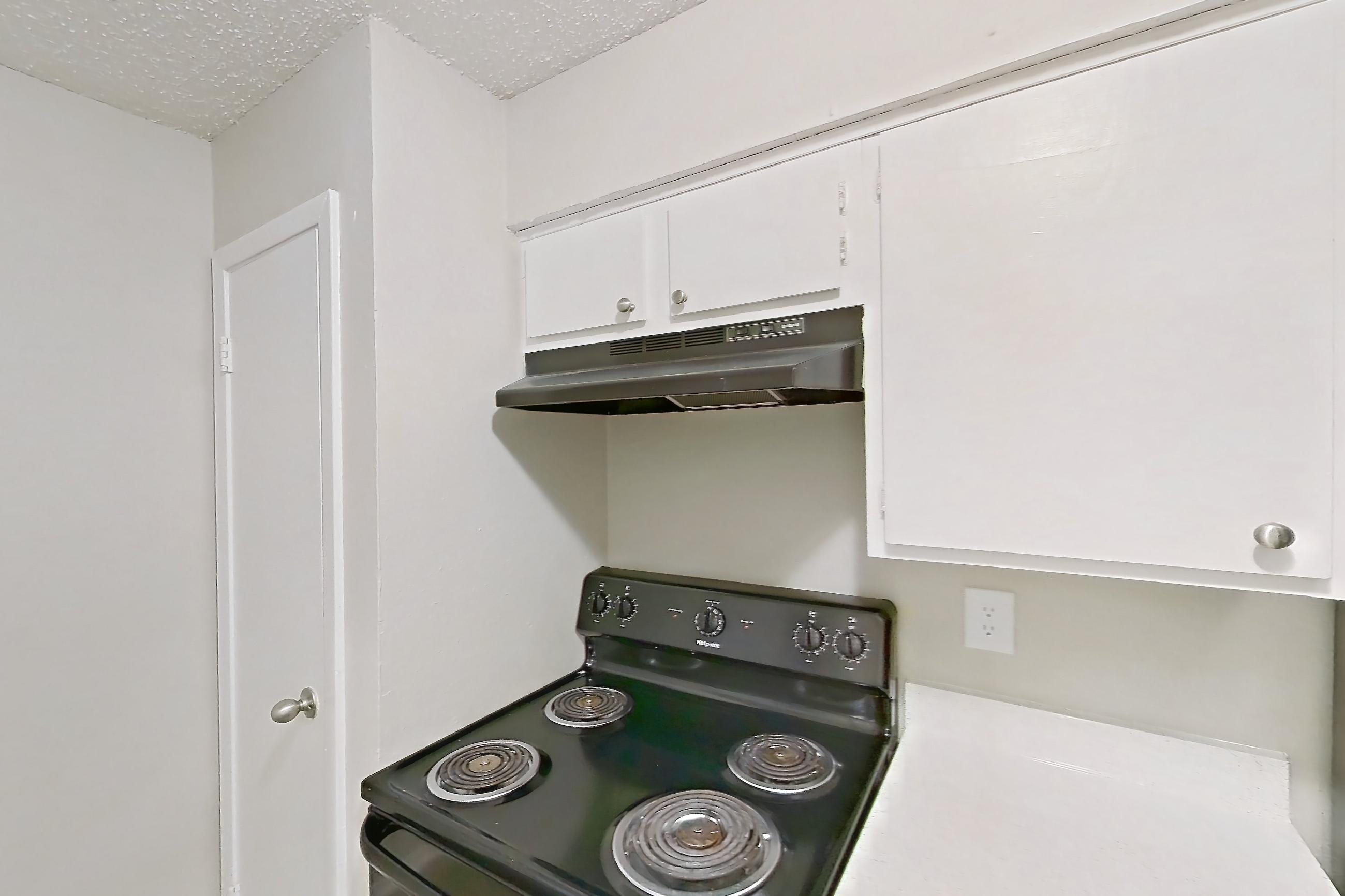 Kitchen with black appliances, dishwasher, electric range, light countertops, light stone countertops, light wood-finish flooring, oven/range, range hood, refrigerator, and stainless steel appliances, Apartment 809 at Westgate