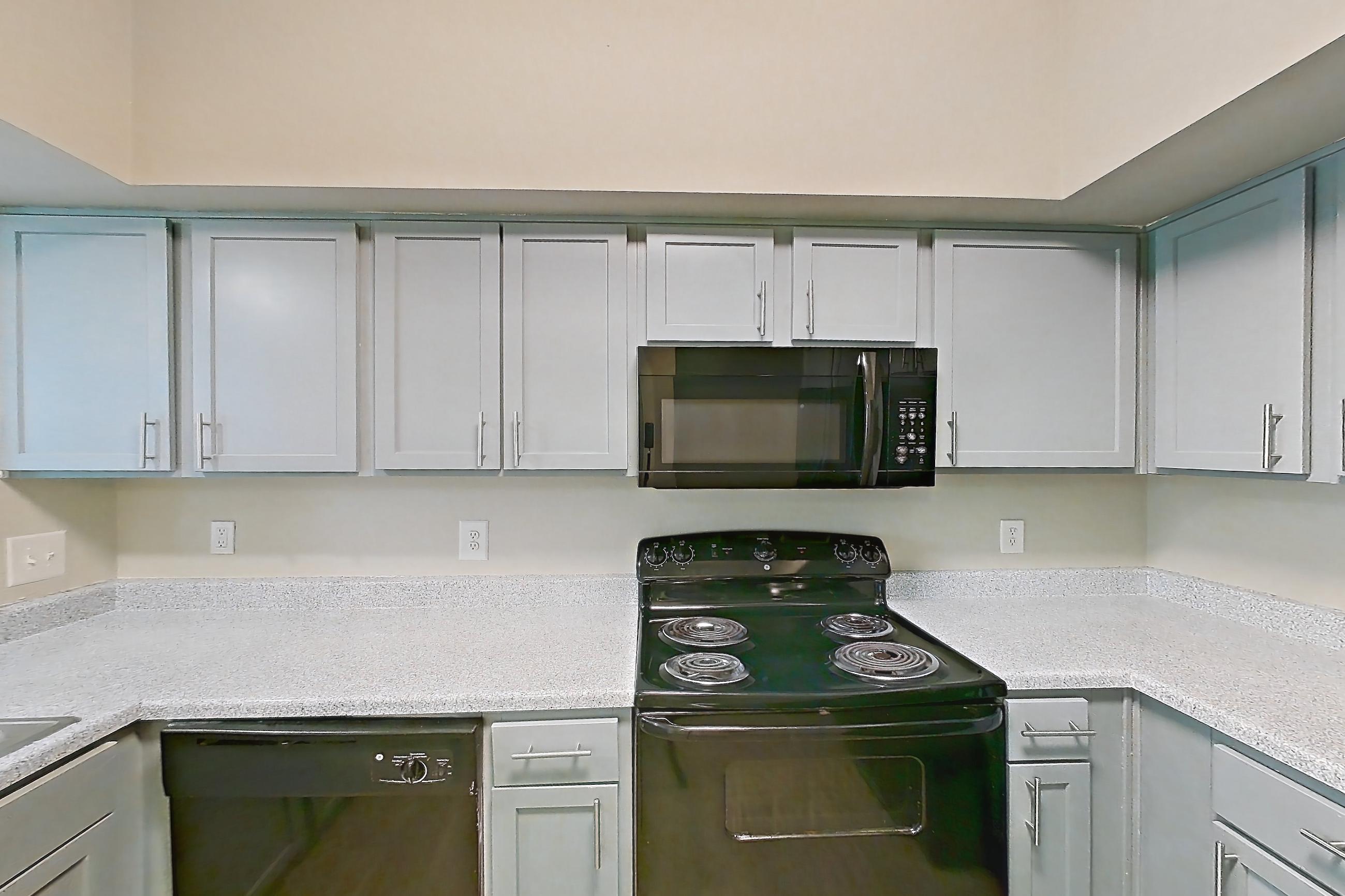 Kitchen with black appliances, dishwasher, electric range, light countertops, light stone countertops, light wood-finish flooring, microwave, oven/range, refrigerator, and water & ice dispenser, Unit 0420 at Champions Park
