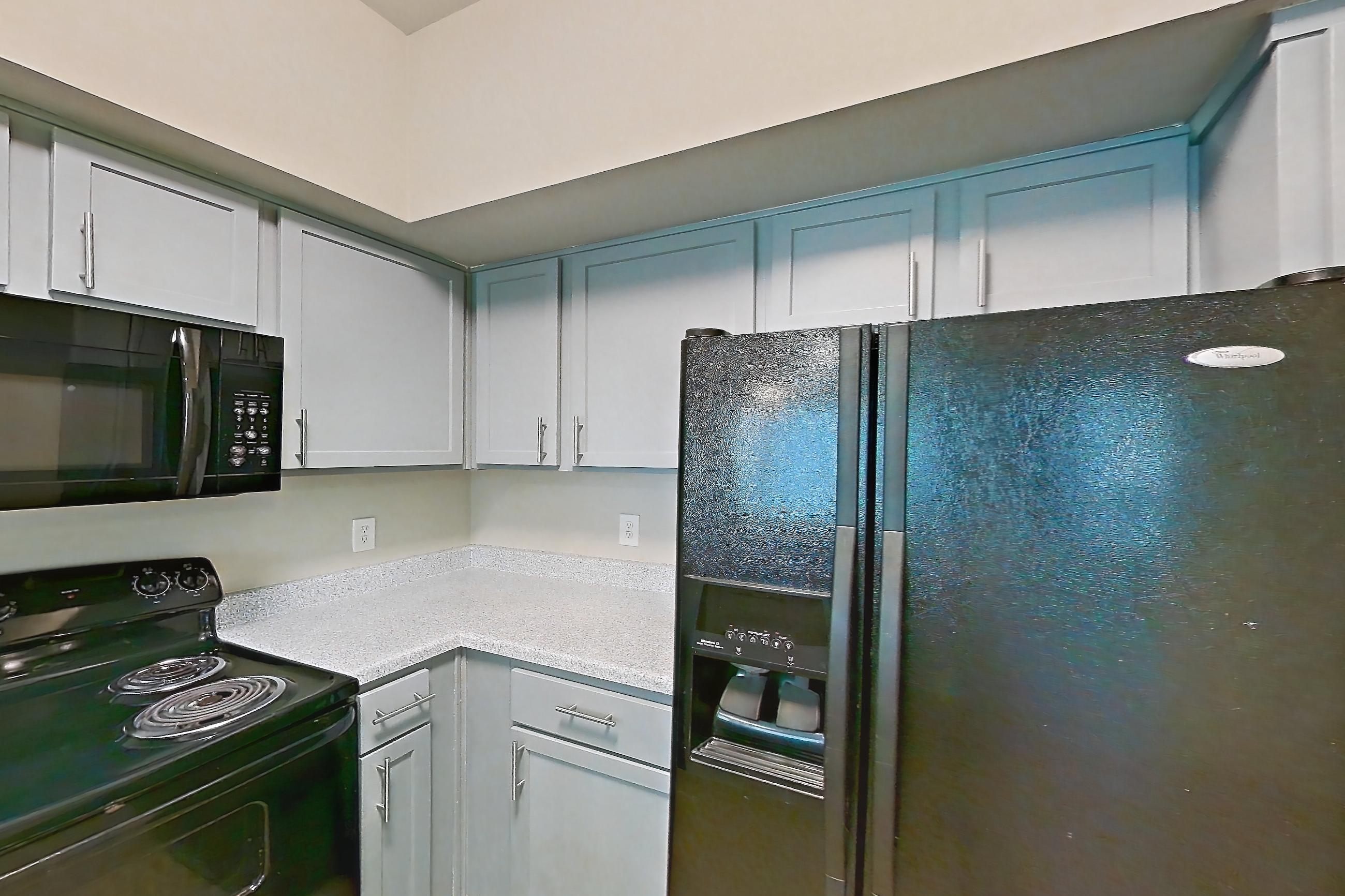Kitchen with black appliances, dishwasher, electric range, light countertops, light stone countertops, light wood-finish flooring, microwave, oven/range, refrigerator, and water & ice dispenser, Unit 0420 at Champions Park