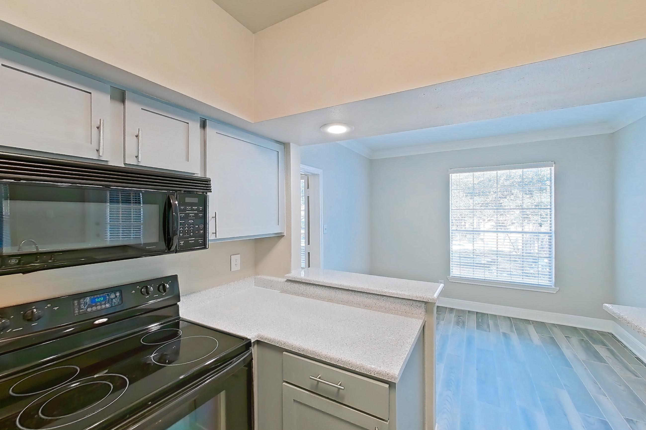 Kitchen with black appliances, dishwasher, electric range, light countertops, light stone countertops, light wood-finish flooring, microwave, oven/range, and wood-look tile flooring, Apartment 0610 at Champions Park