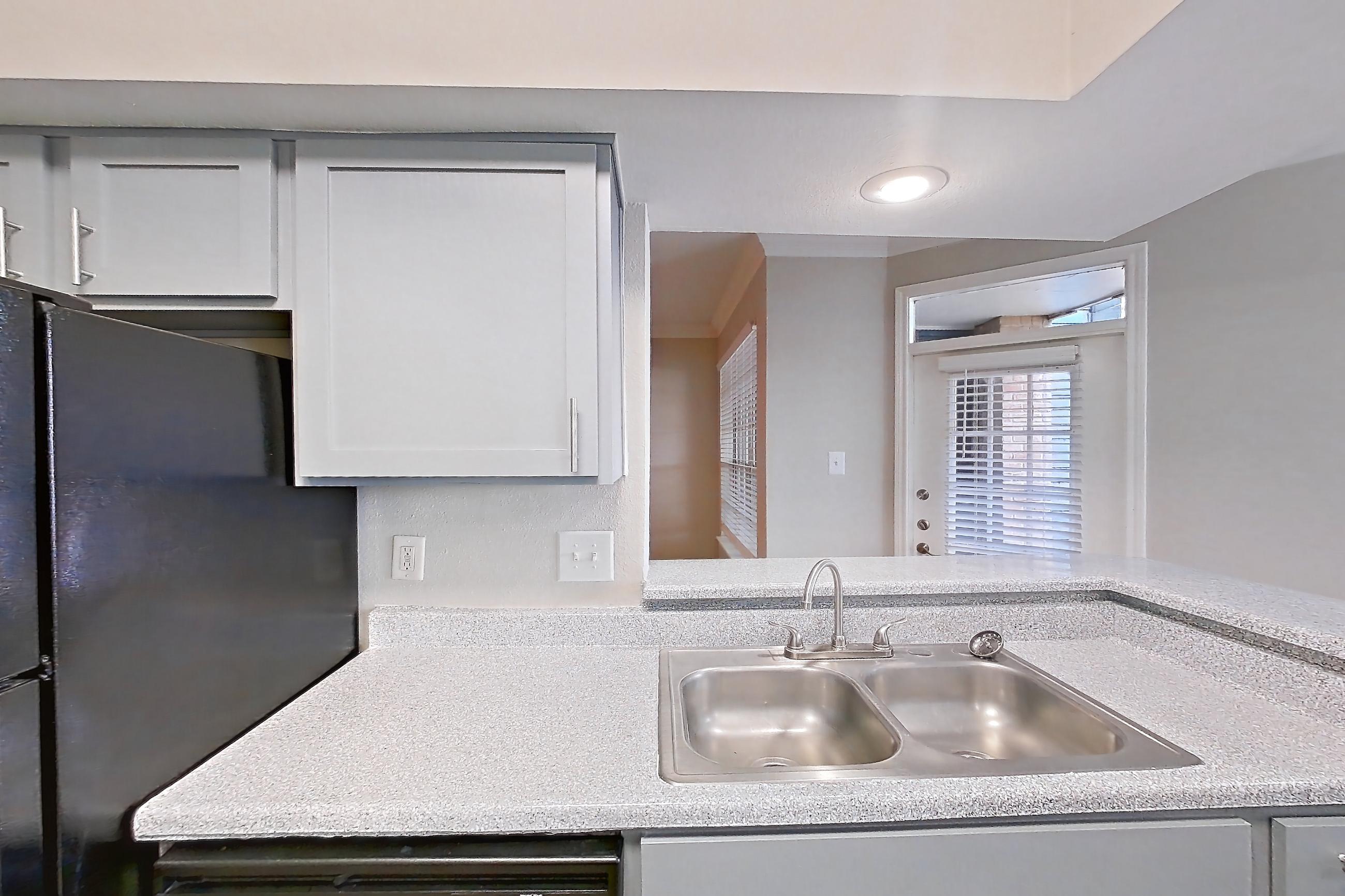 Kitchen with black appliances, dark wood-finish flooring, dishwasher, light countertops, light stone countertops, light wood-finish flooring, refrigerator, and wood-look tile flooring, Unit 0917 at Champions Park
