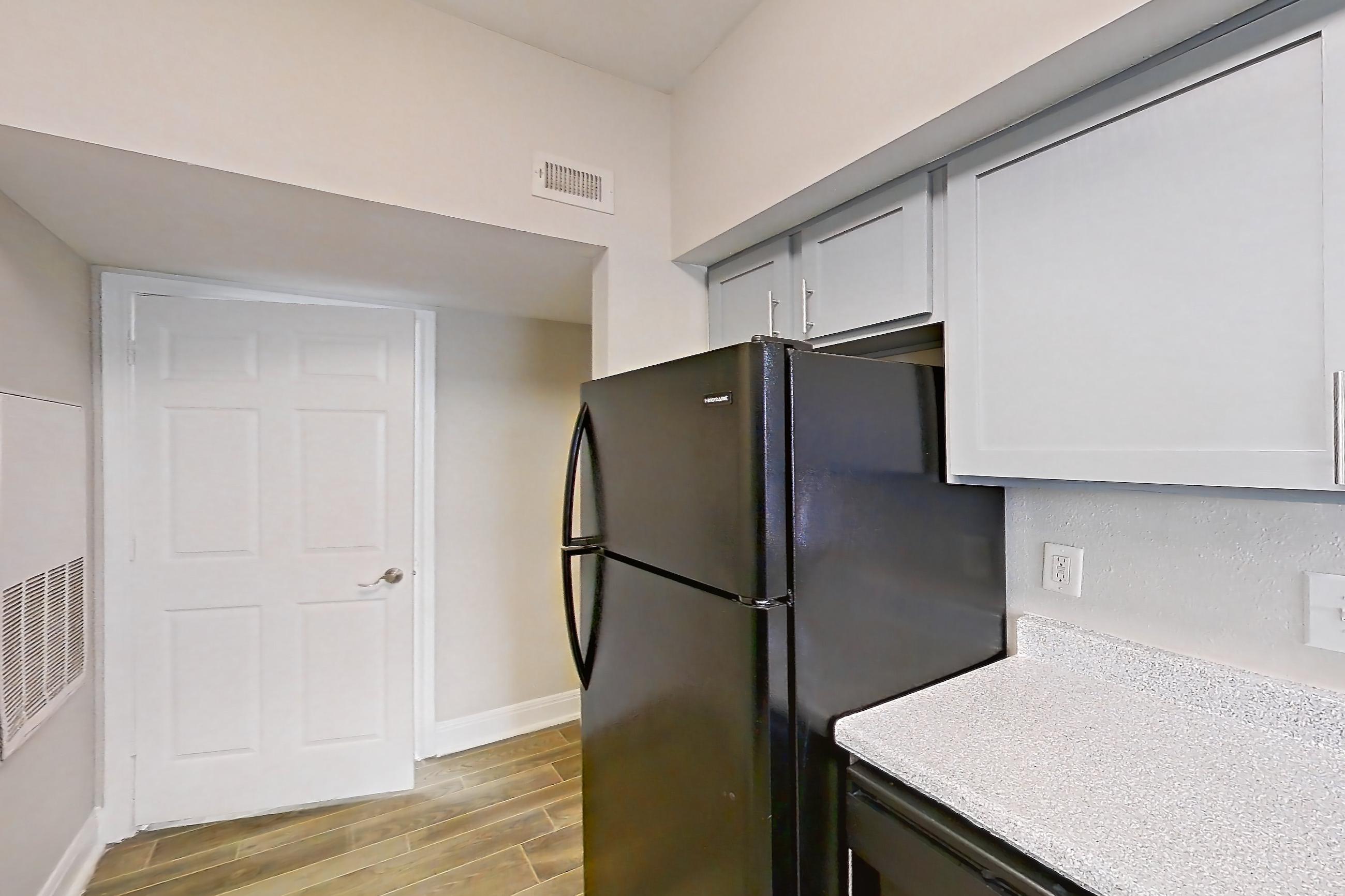 Kitchen with black appliances, dark wood-finish flooring, dishwasher, light countertops, light stone countertops, light wood-finish flooring, refrigerator, and wood-look tile flooring, Unit 0917 at Champions Park