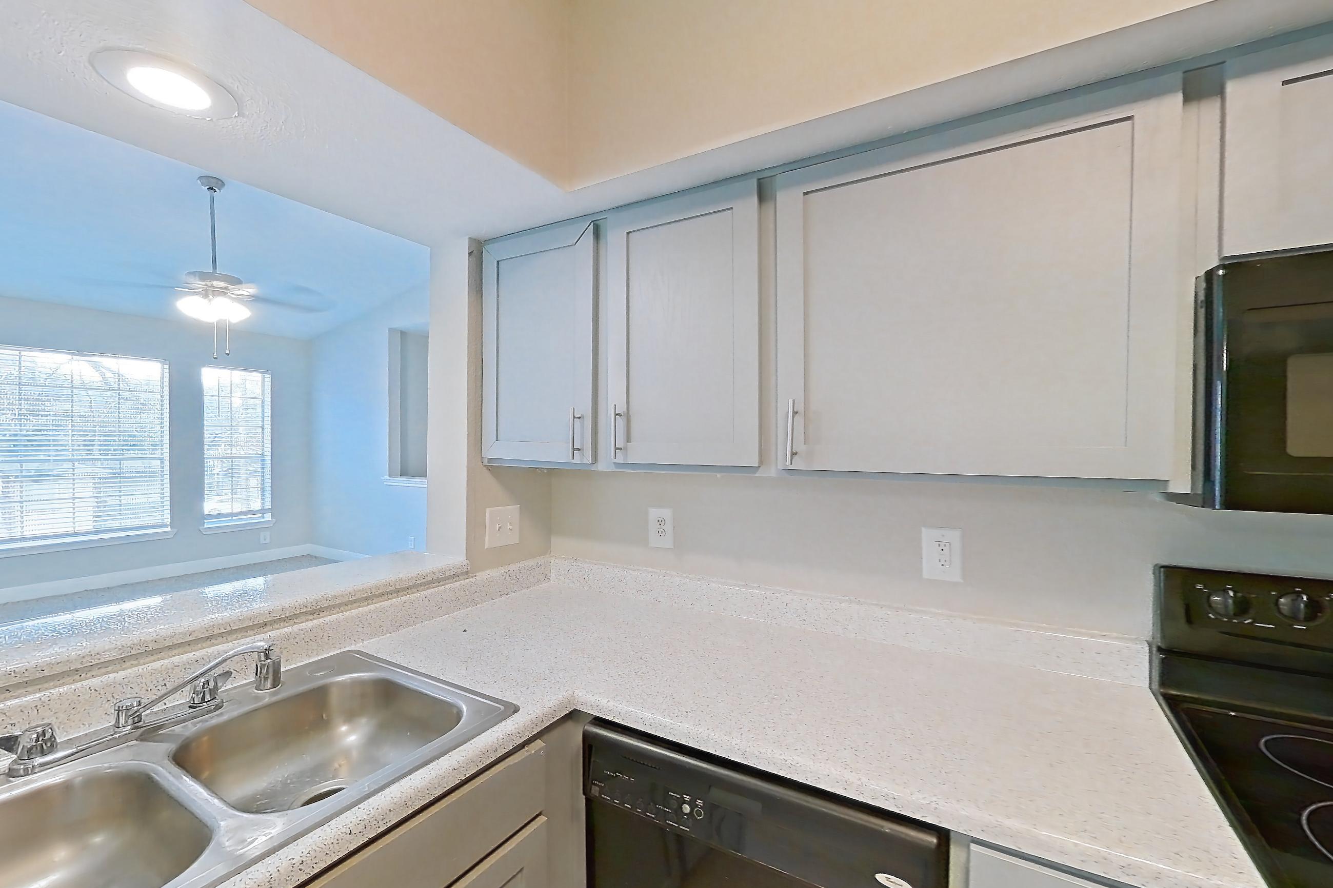 Kitchen with black appliances, dishwasher, electric range, in-unit laundry, light countertops, light stone countertops, light wood-finish flooring, microwave, and oven/range, Unit 1202 at Champions Park