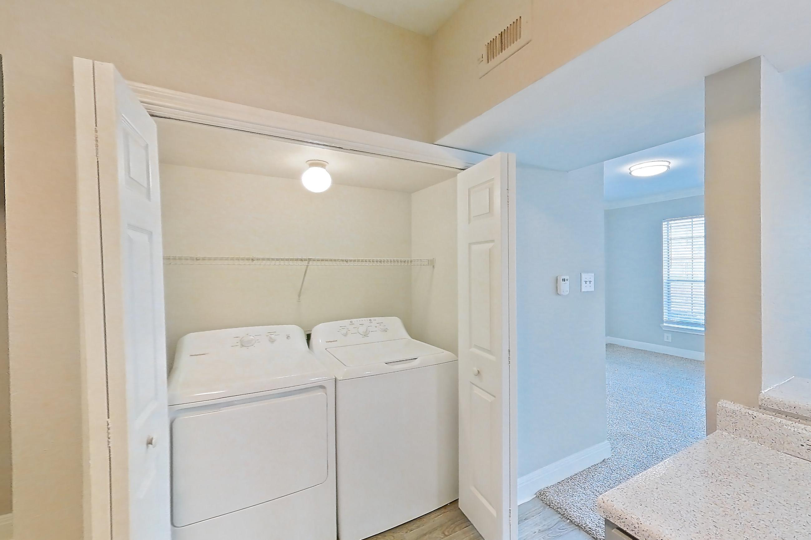 Kitchen with black appliances, dishwasher, electric range, in-unit laundry, light countertops, light stone countertops, light wood-finish flooring, microwave, and oven/range, Unit 1202 at Champions Park