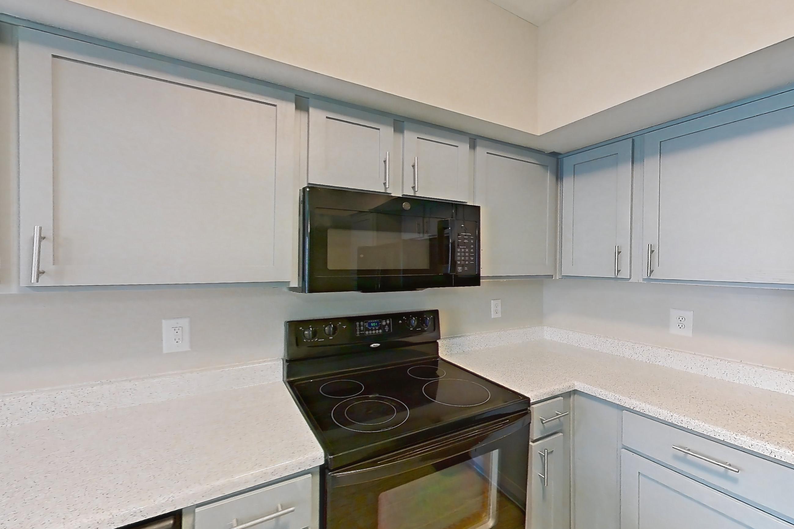 Kitchen with black appliances, dishwasher, electric range, in-unit laundry, light countertops, light stone countertops, light wood-finish flooring, microwave, and oven/range, Unit 1202 at Champions Park