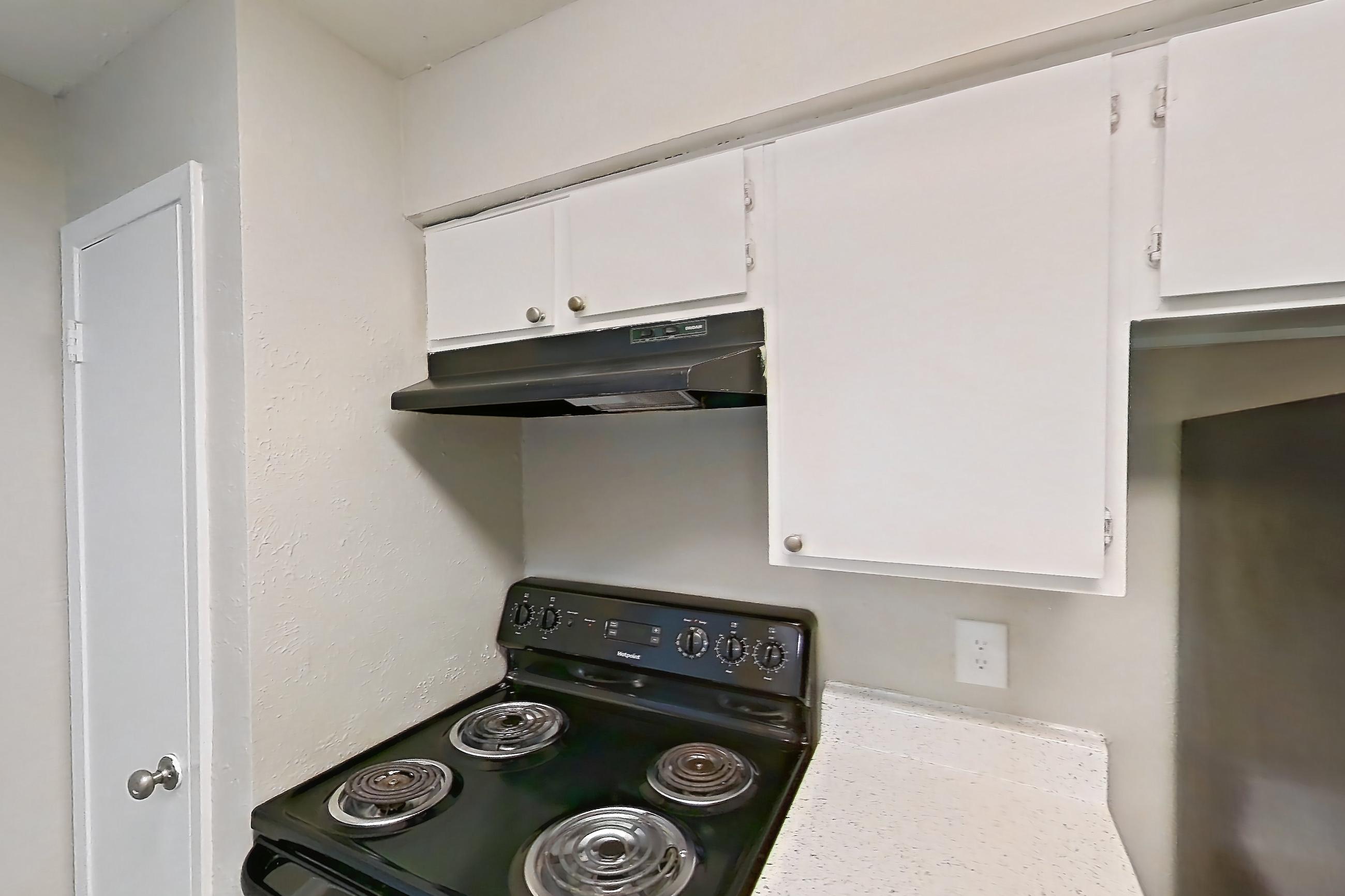 Kitchen with black appliances, dishwasher, electric range, light countertops, light stone countertops, light wood-finish flooring, oven/range, and refrigerator, Apartment 2121 at Westgate