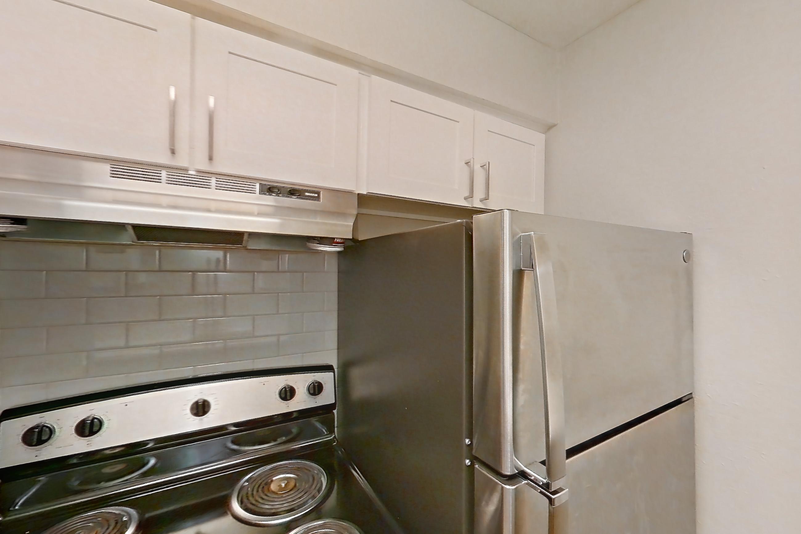 Kitchen with black appliances, cooktop, electric cooktop, electric range, light countertops, light stone countertops, light wood-finish flooring, oven/range, range hood, refrigerator, and stainless steel appliances, Apartment 10 at Loreto Apartment Homes