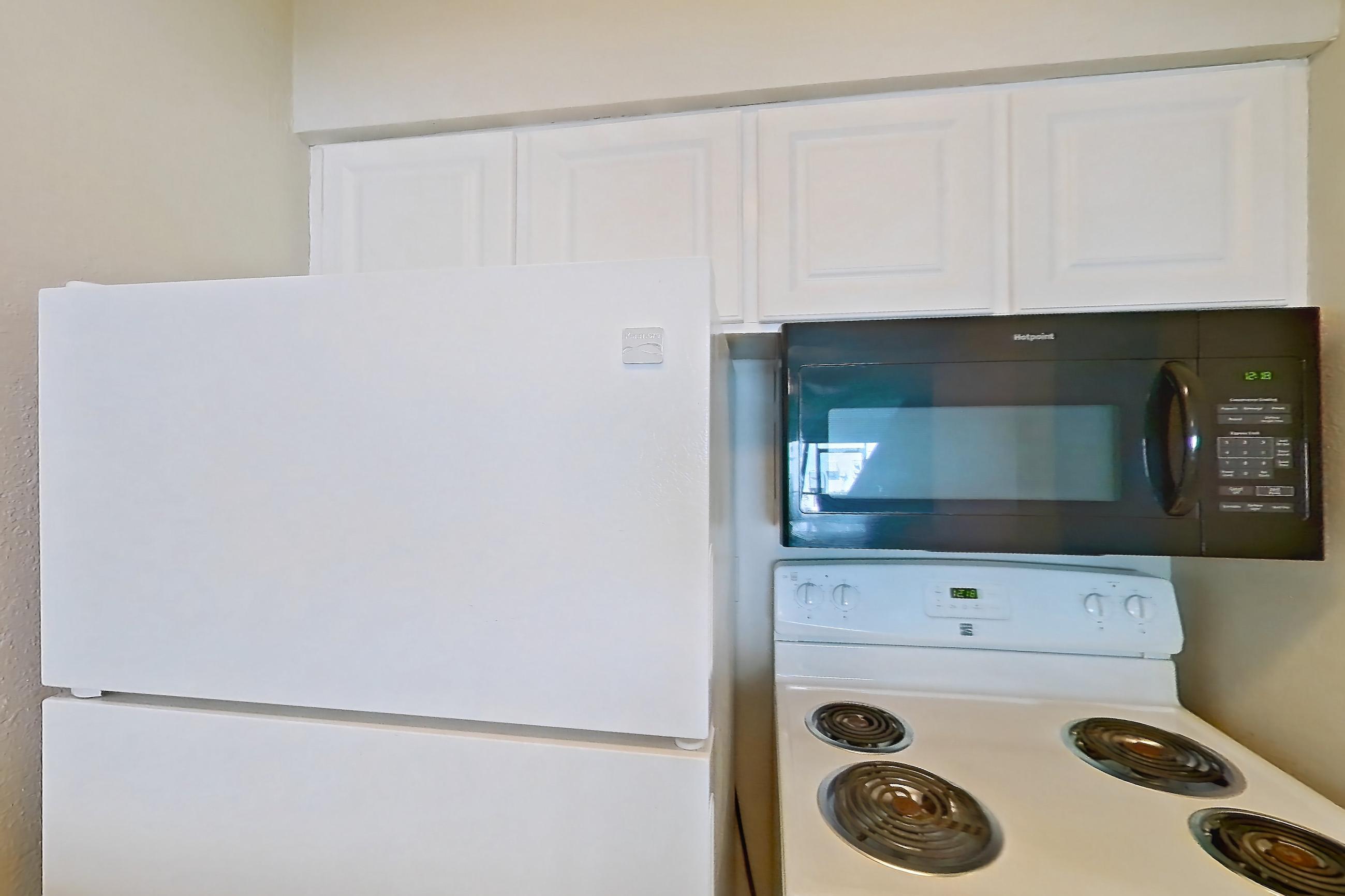Kitchen with black appliances, electric range, light countertops, light stone countertops, light wood-finish flooring, microwave, oven/range, refrigerator, and white appliances, Apartment C-88 at Sunset Place