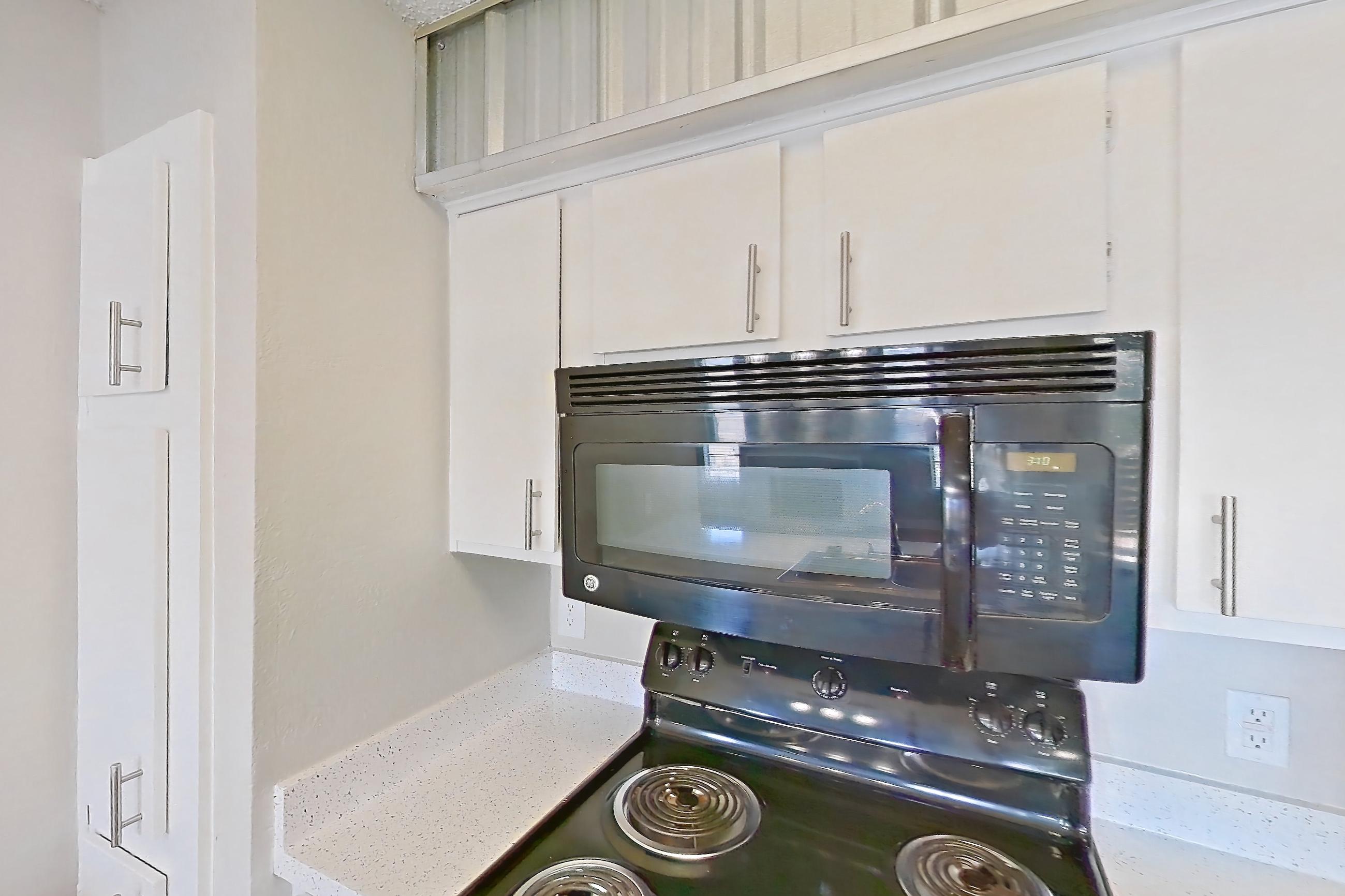 Kitchen with black appliances, dishwasher, electric range, fireplace, light countertops, light stone countertops, light wood-finish flooring, microwave, oven/range, refrigerator, stainless steel appliances, and wood-look tile flooring, Apartment 232 at Sedona Park