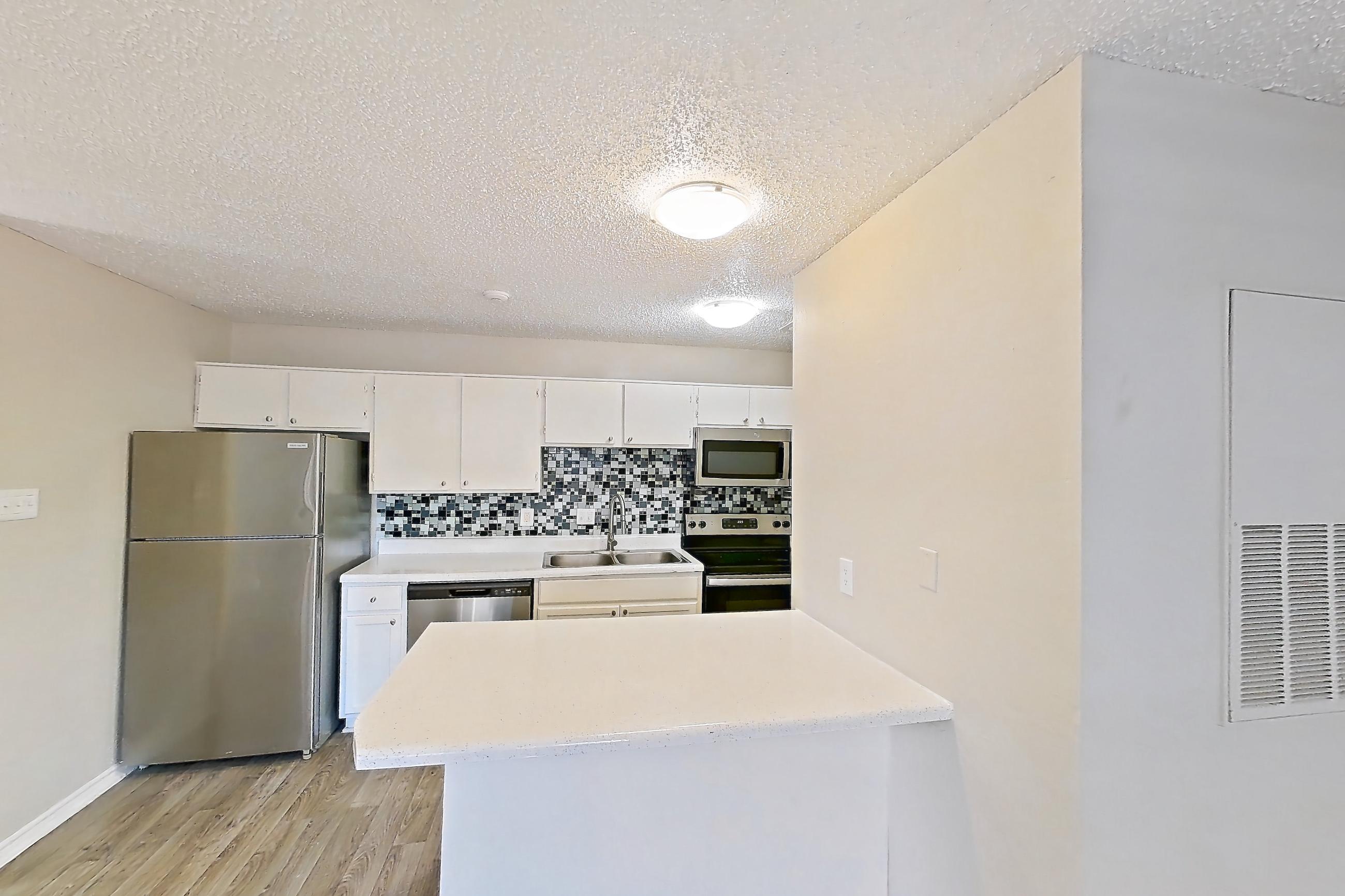 Living room with dishwasher, electric range, light countertops, light wood-finish flooring, oven/range, refrigerator, and stainless steel appliances, Apartment 1601P at The Carmel
