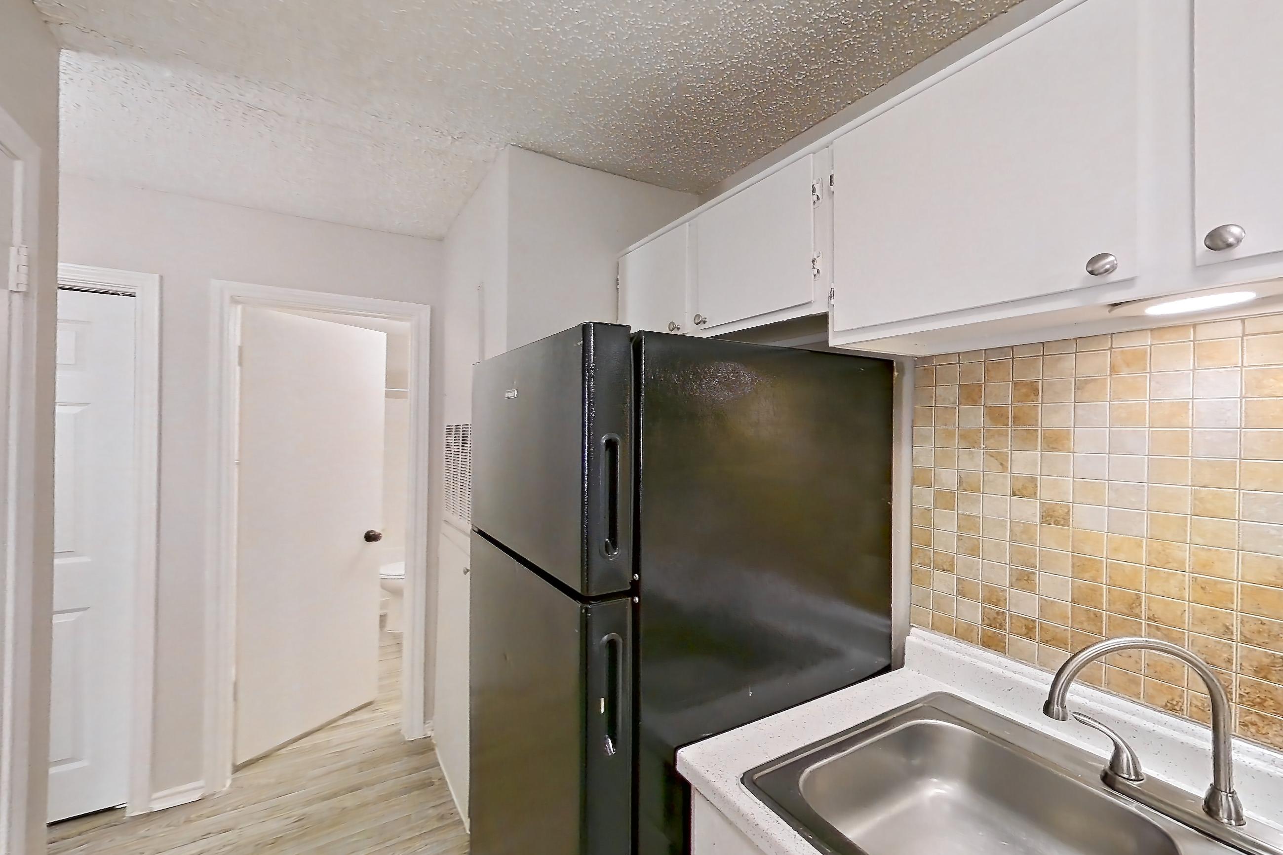 Kitchen with black appliances, dishwasher, electric range, light countertops, light stone countertops, light wood-finish flooring, oven/range, range hood, and refrigerator, Apartment 1605P at The Carmel