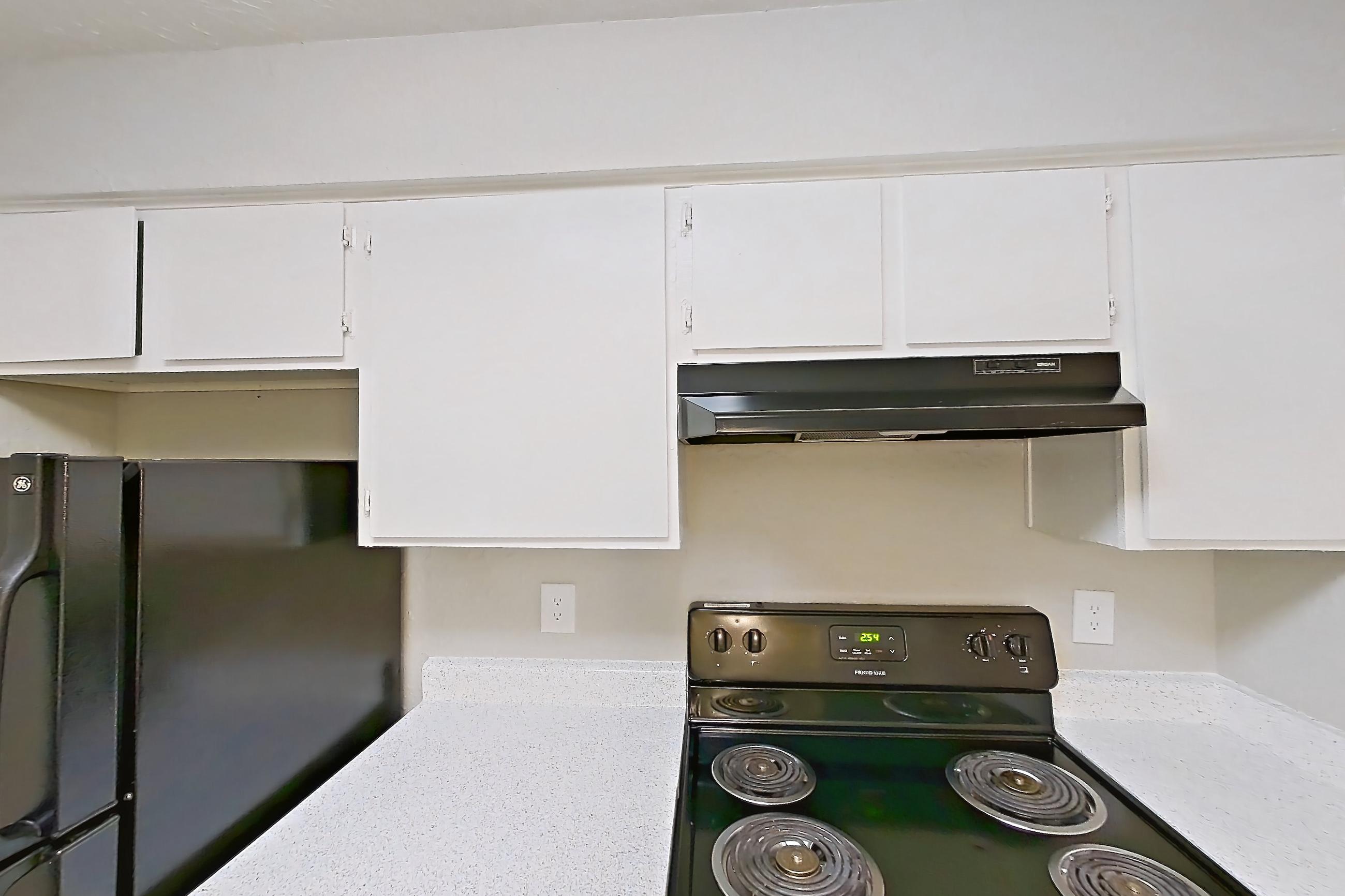 Kitchen with black appliances, electric range, light countertops, light stone countertops, light wood-finish flooring, oven/range, and refrigerator, Apartment 118B at The Carmel