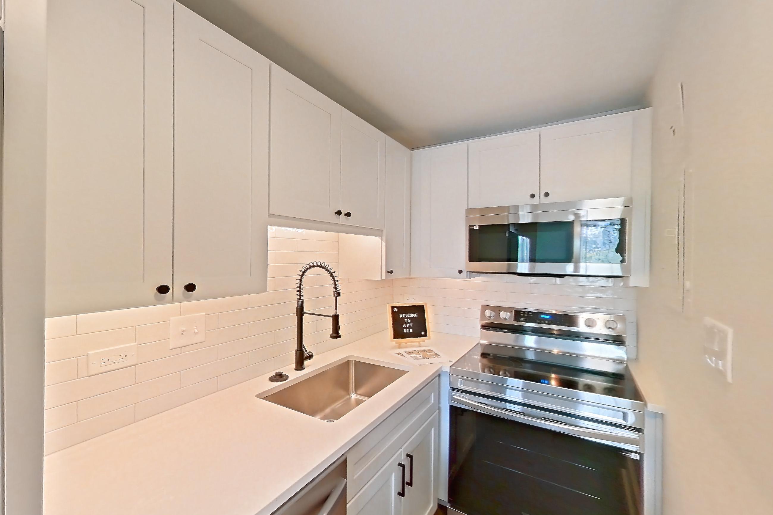 Kitchen with dark wood-finish flooring, dishwasher, electric range, light countertops, light stone countertops, microwave, oven/range, refrigerator, and stainless steel appliances, Apartment 316 at Cortland at McLean