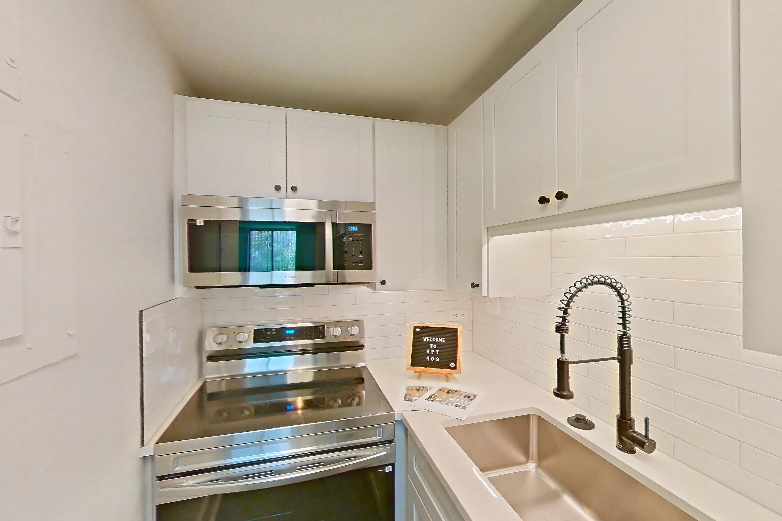 Kitchen with dark wood-finish flooring, electric range, light countertops, light stone countertops, microwave, oven/range, and stainless steel appliances, Apartment 409 at Cortland at McLean