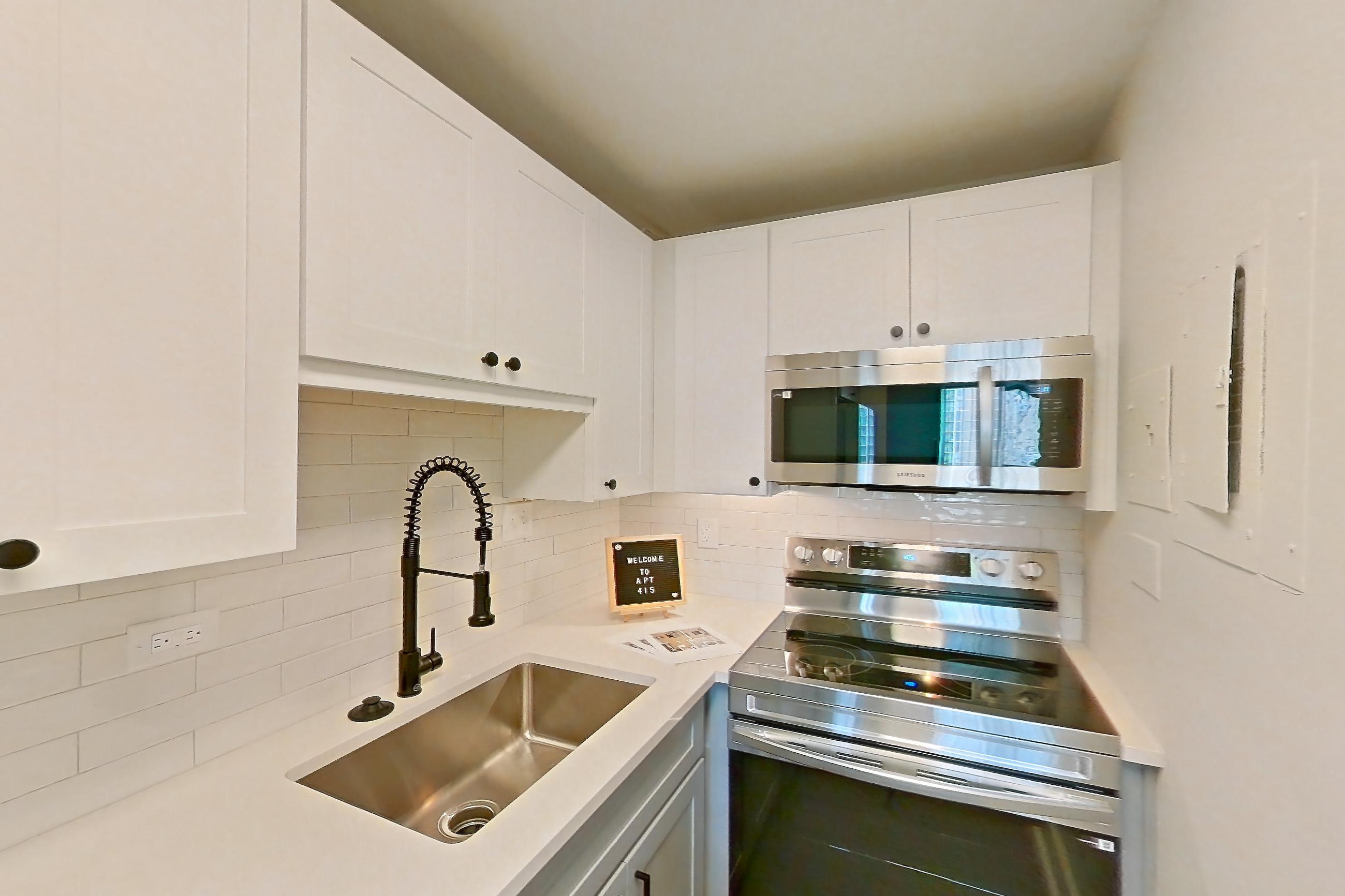 Kitchen with dark wood-finish flooring, dishwasher, electric range, light countertops, light stone countertops, microwave, oven/range, and stainless steel appliances, Apartment 415 at Cortland at McLean