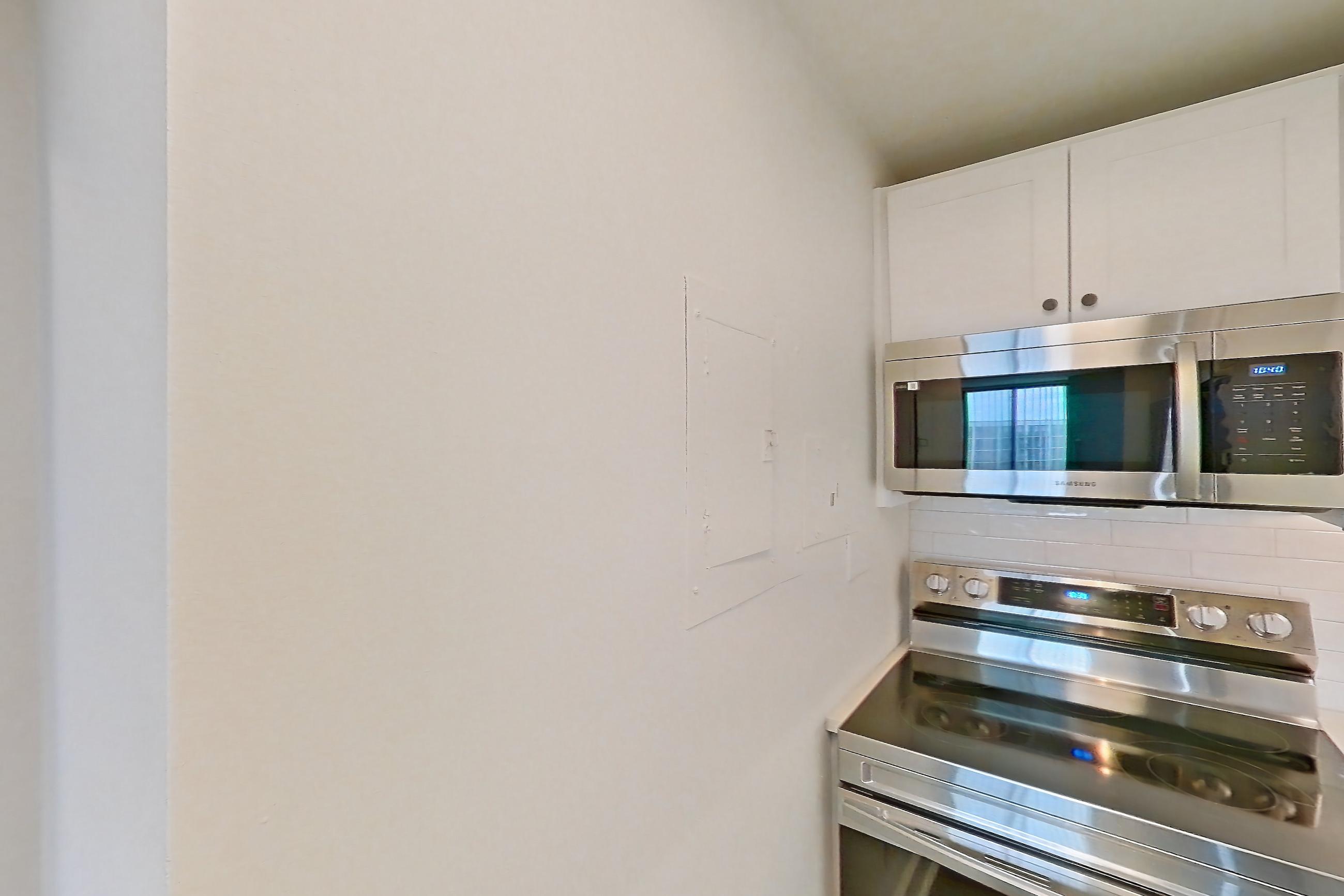Kitchen with dark wood-finish flooring, dishwasher, electric range, light countertops, light stone countertops, microwave, oven/range, and stainless steel appliances, Apartment 909 at Cortland at McLean