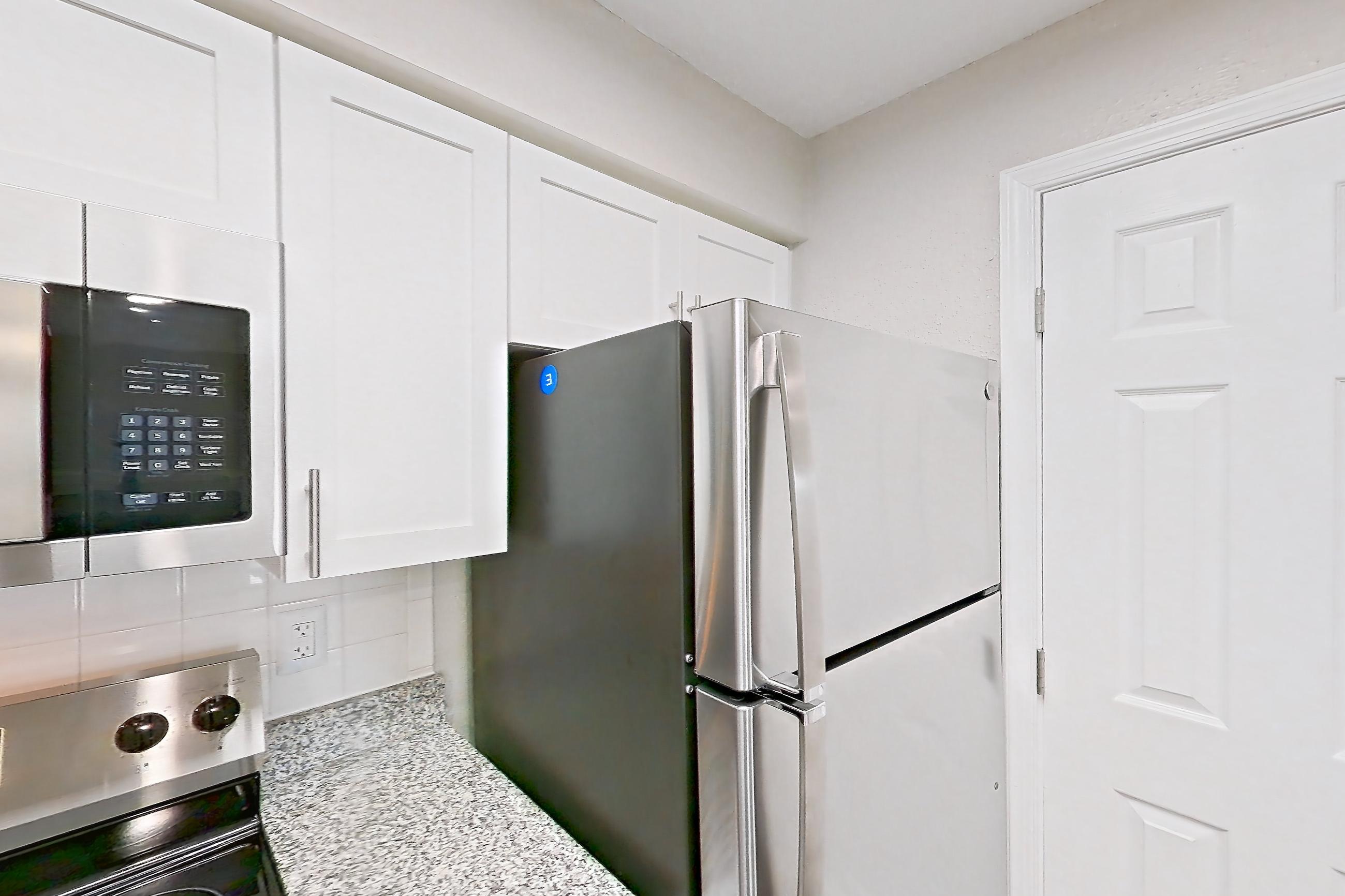 Kitchen with dishwasher, electric range, fireplace, light countertops, light stone countertops, light wood-finish flooring, microwave, oven/range, refrigerator, stainless steel appliances, and tile fireplace, Apartment 4206 at Cortland Van Dorn