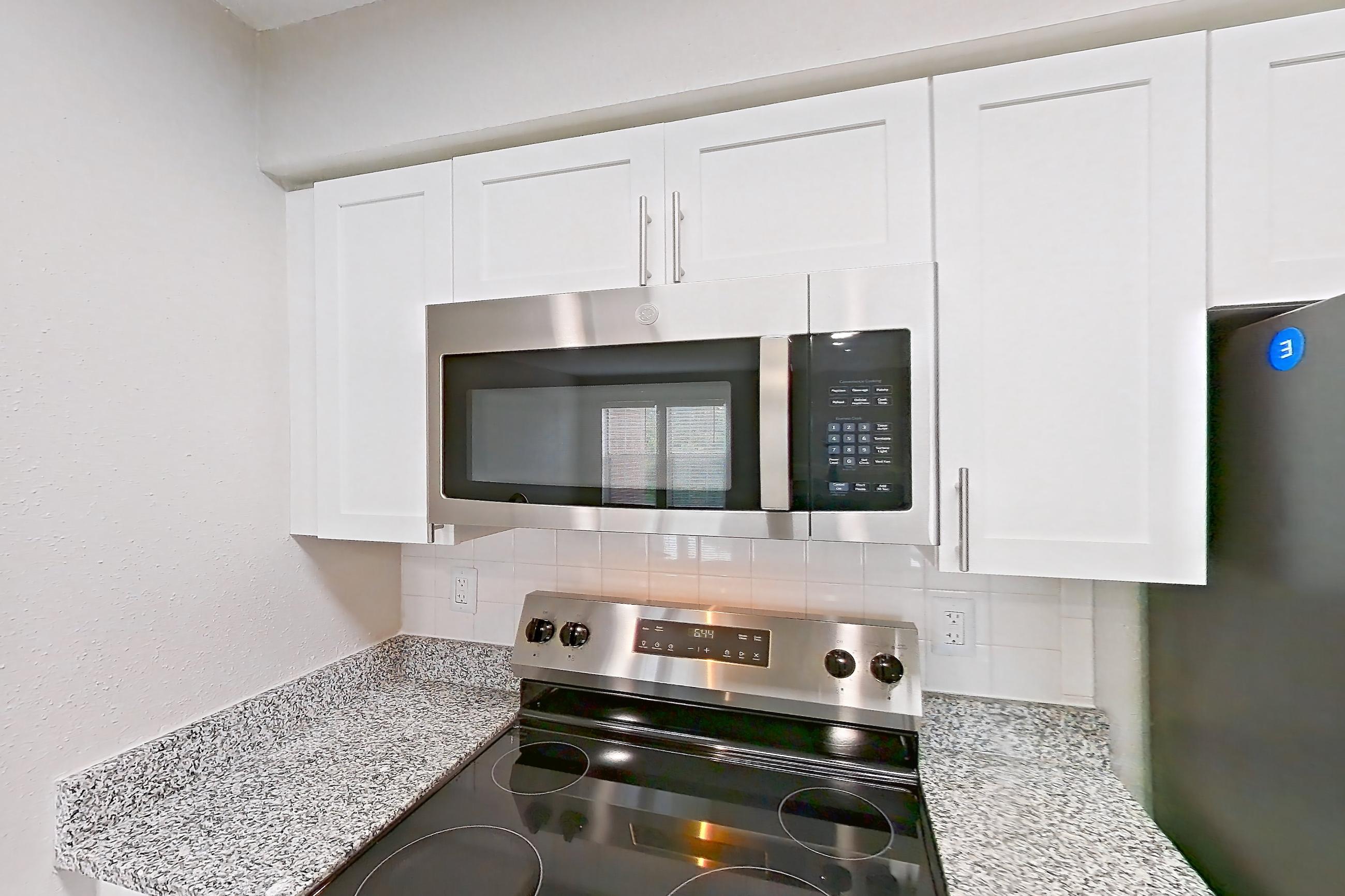 Kitchen with dishwasher, electric range, fireplace, light countertops, light stone countertops, light wood-finish flooring, microwave, oven/range, refrigerator, stainless steel appliances, and tile fireplace, Apartment 4206 at Cortland Van Dorn