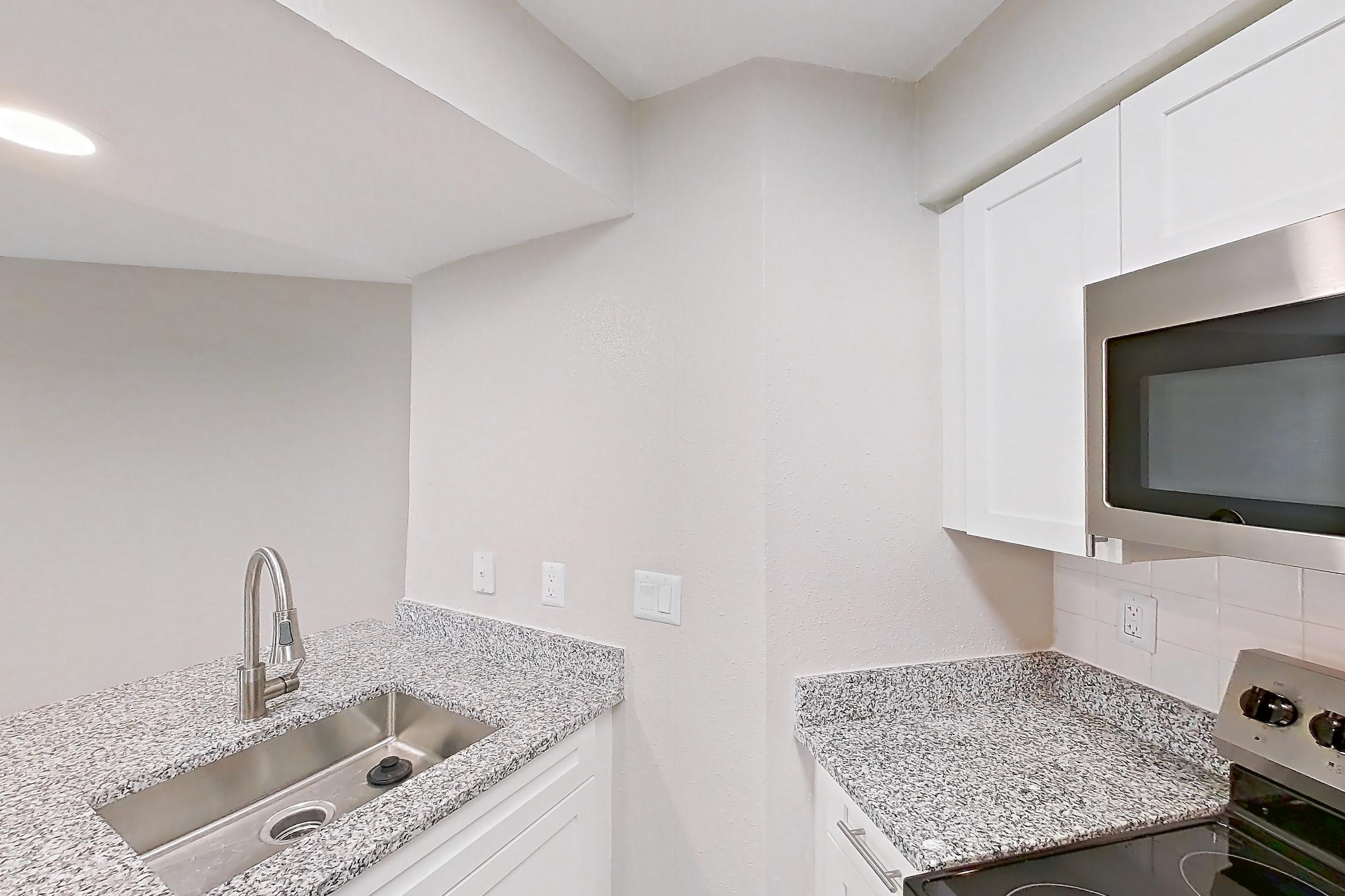 Kitchen with dishwasher, electric range, fireplace, light countertops, light stone countertops, light wood-finish flooring, microwave, oven/range, refrigerator, stainless steel appliances, and tile fireplace, Apartment 4206 at Cortland Van Dorn