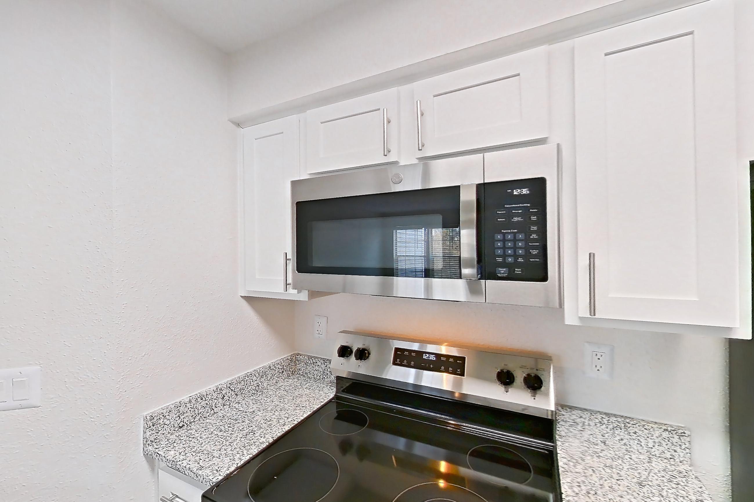 Kitchen with dishwasher, electric range, fireplace, light countertops, light stone countertops, light wood-finish flooring, microwave, oven/range, refrigerator, stainless steel appliances, and tile fireplace, Apartment 7305 at Cortland Van Dorn