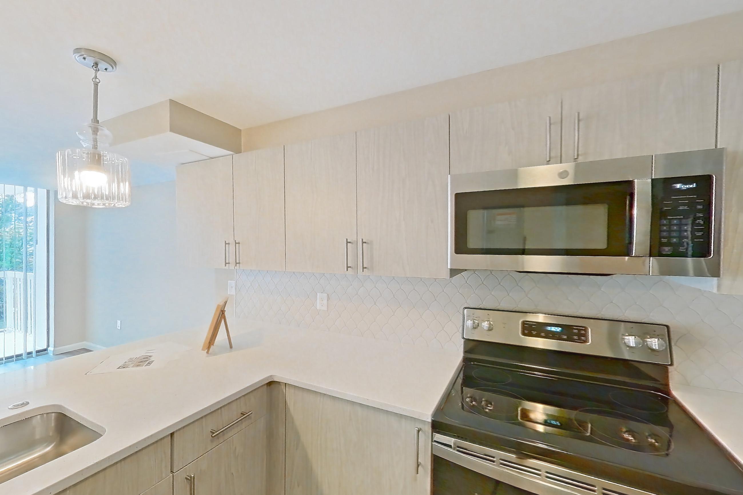 Kitchen with dishwasher, electric range, light countertops, light stone countertops, light wood-finish flooring, microwave, oven/range, refrigerator, and stainless steel appliances, Apartment 219 at Cortland at McLean