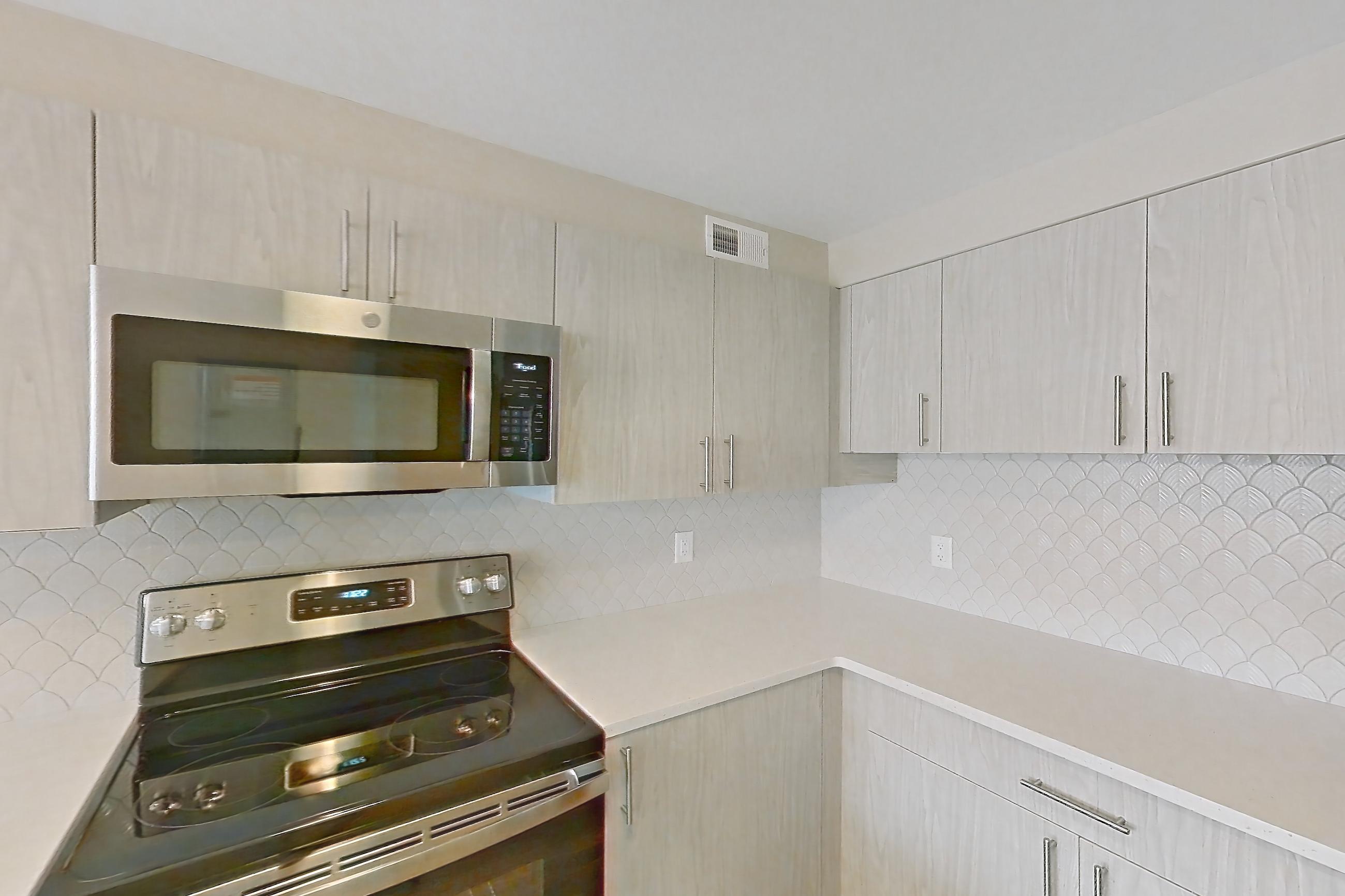 Kitchen with dishwasher, electric range, light countertops, light stone countertops, light wood-finish flooring, microwave, oven/range, refrigerator, and stainless steel appliances, Apartment 219 at Cortland at McLean