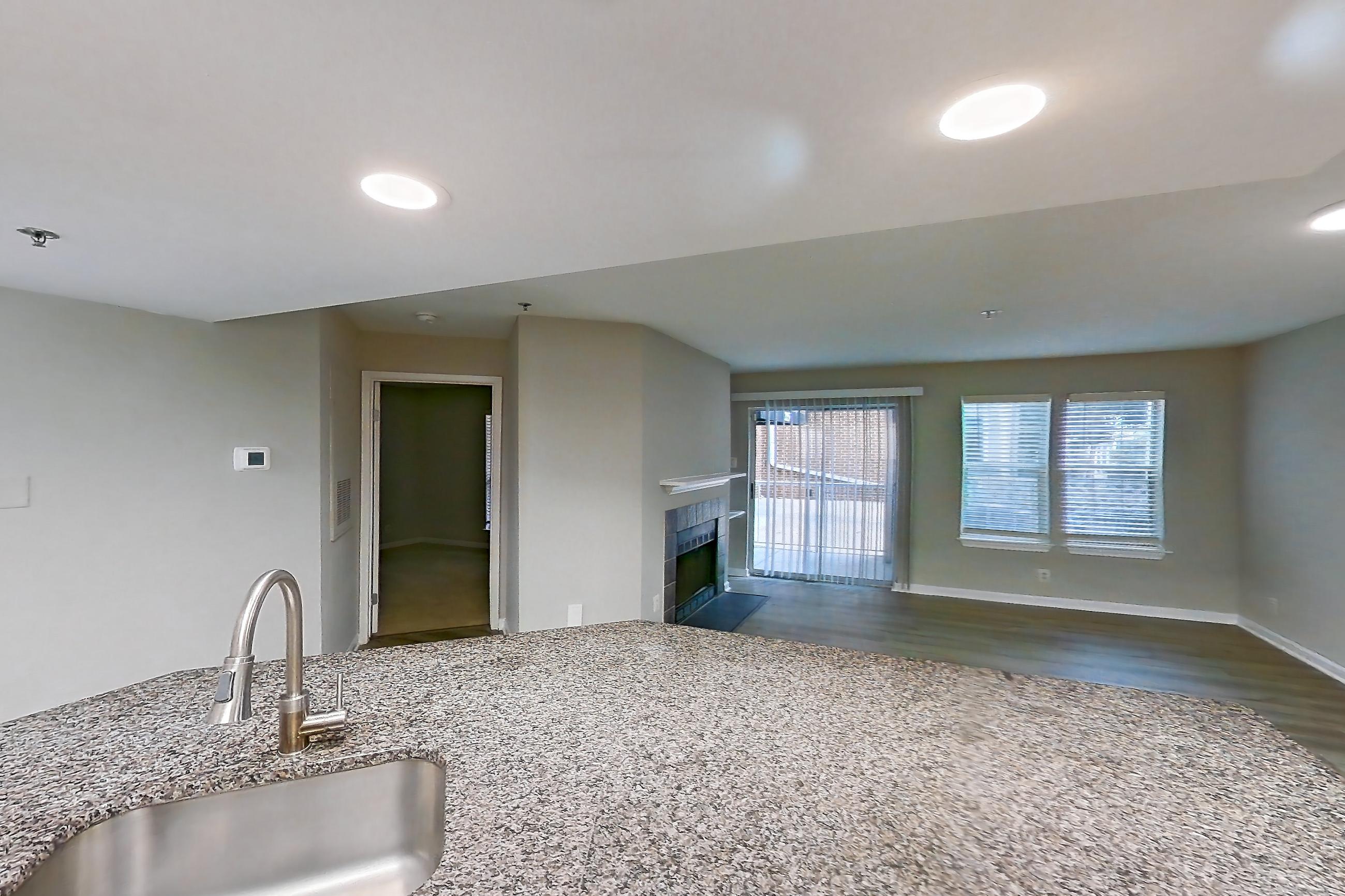 Kitchen with dark stone countertops, dishwasher, electric range, fireplace, light countertops, light stone countertops, light wood-finish flooring, microwave, oven/range, refrigerator, stainless steel appliances, and tile fireplace, Apartment 1101 at Cortland Van Dorn