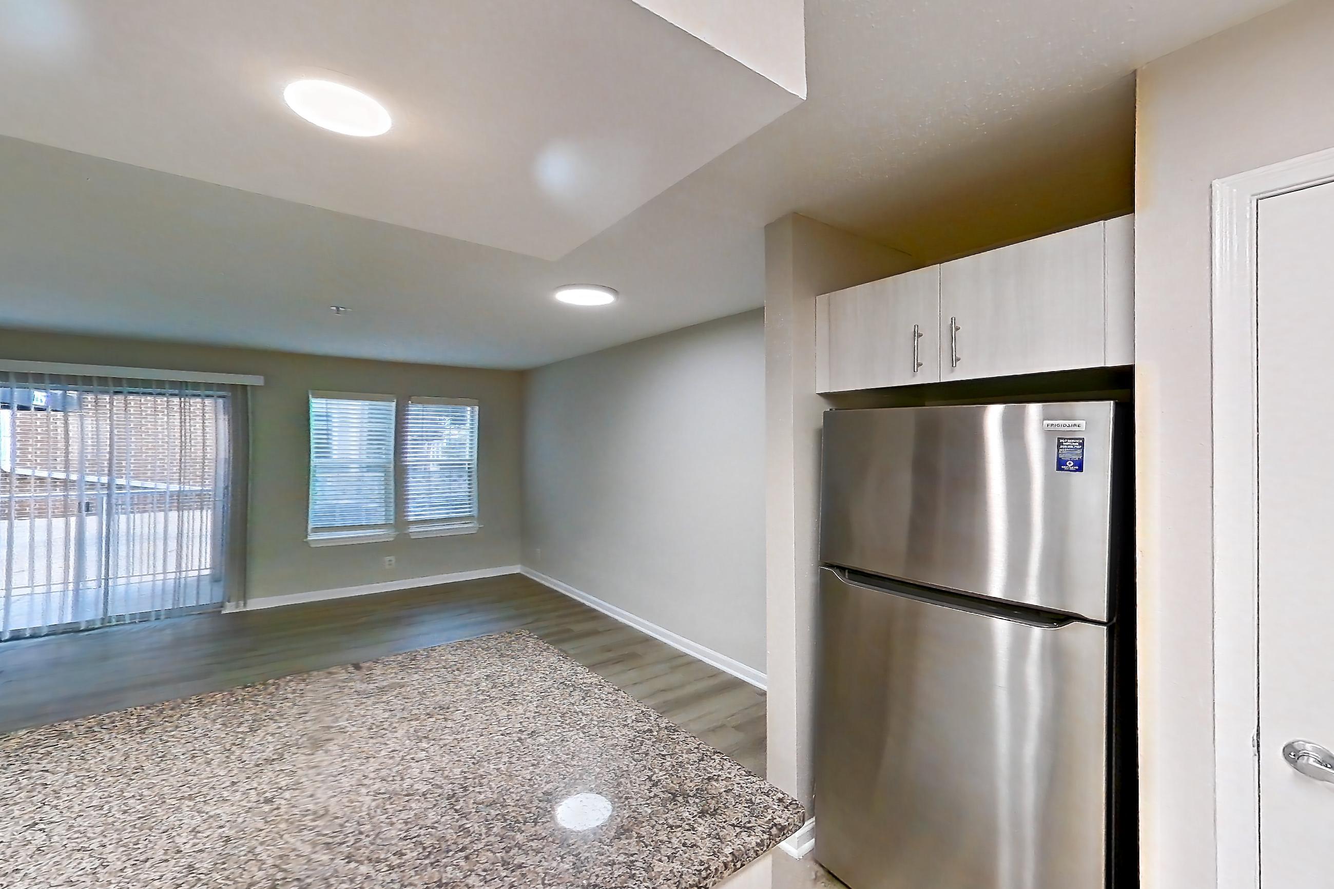 Kitchen with dark stone countertops, dishwasher, electric range, fireplace, light countertops, light stone countertops, light wood-finish flooring, microwave, oven/range, refrigerator, stainless steel appliances, and tile fireplace, Apartment 1101 at Cortland Van Dorn