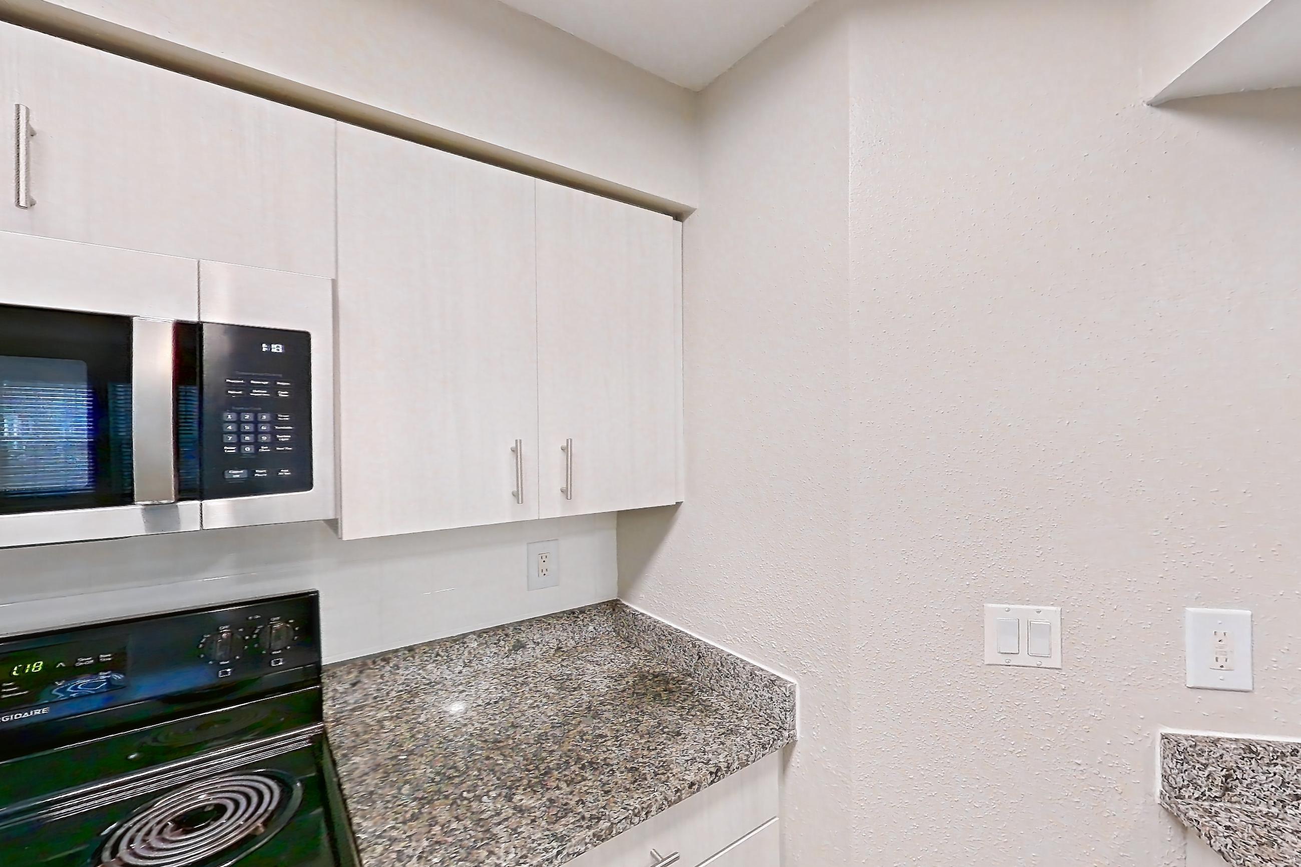Kitchen with dark stone countertops, dishwasher, electric range, fireplace, light countertops, light stone countertops, light wood-finish flooring, microwave, oven/range, refrigerator, stainless steel appliances, and tile fireplace, Apartment 1101 at Cortland Van Dorn
