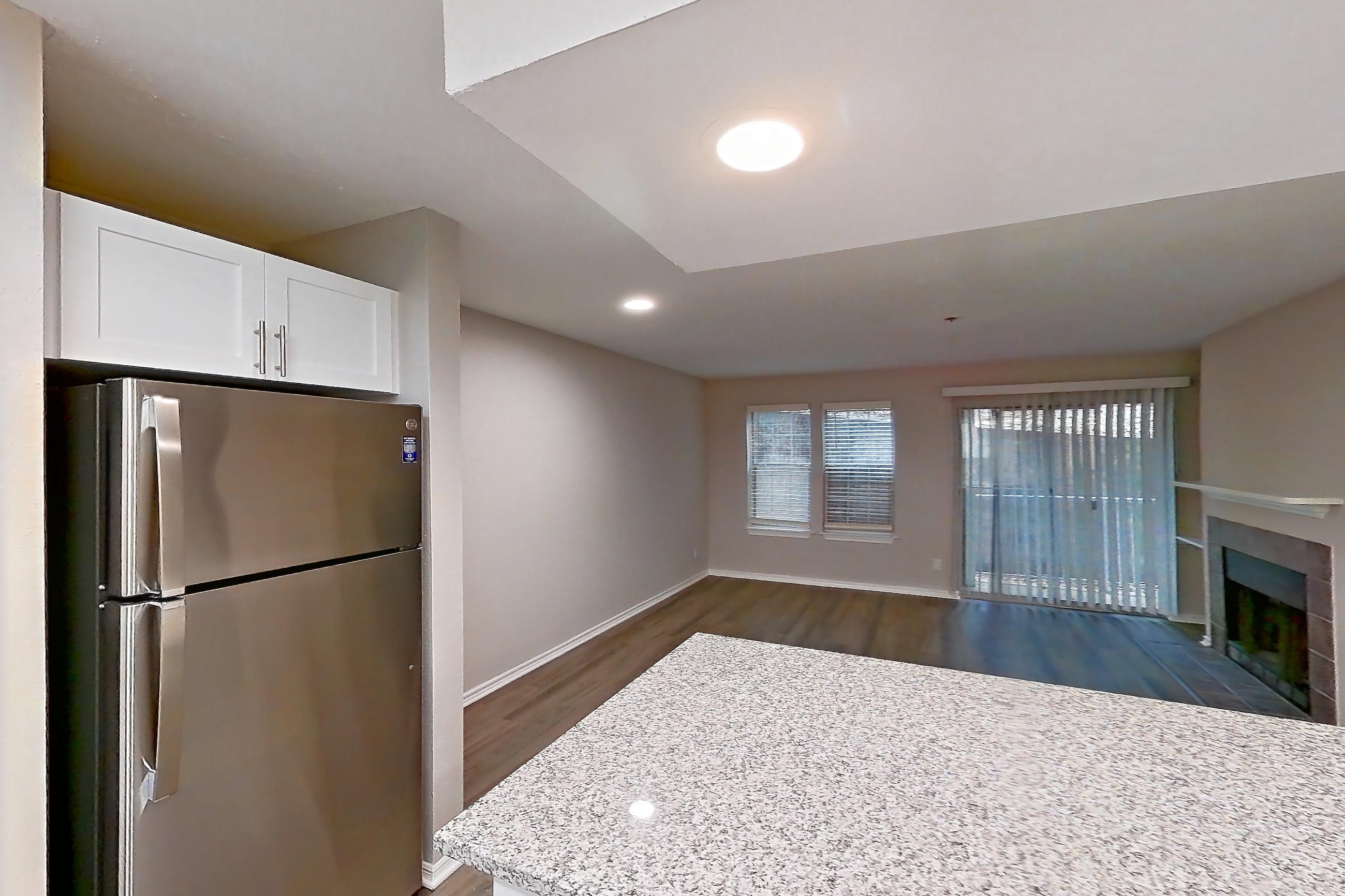 Kitchen with dark wood-finish flooring, dishwasher, electric range, fireplace, light countertops, light stone countertops, light wood-finish flooring, microwave, oven/range, and stainless steel appliances, Apartment 3110 at Cortland Van Dorn