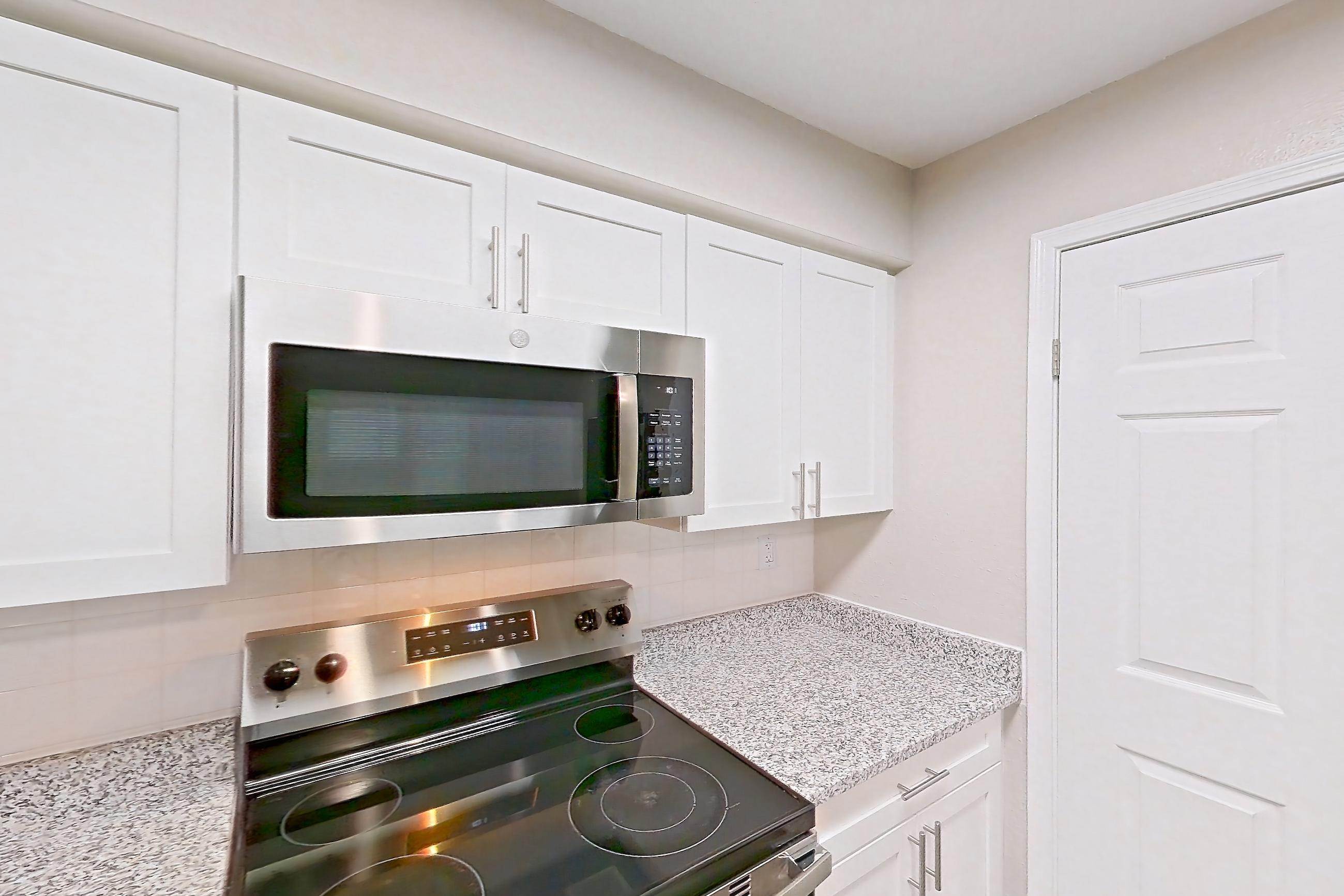 Kitchen with dark wood-finish flooring, dishwasher, electric range, fireplace, light countertops, light stone countertops, light wood-finish flooring, microwave, oven/range, and stainless steel appliances, Apartment 3110 at Cortland Van Dorn