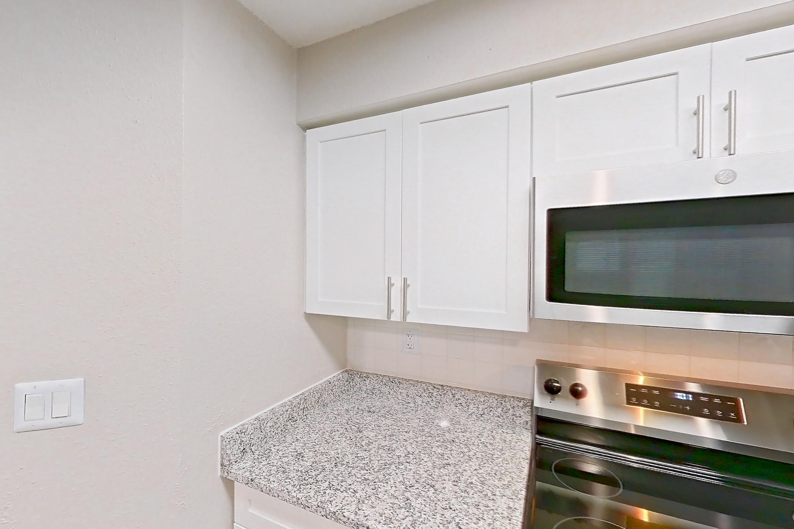 Kitchen with dark wood-finish flooring, dishwasher, electric range, fireplace, light countertops, light stone countertops, light wood-finish flooring, microwave, oven/range, and stainless steel appliances, Apartment 3110 at Cortland Van Dorn